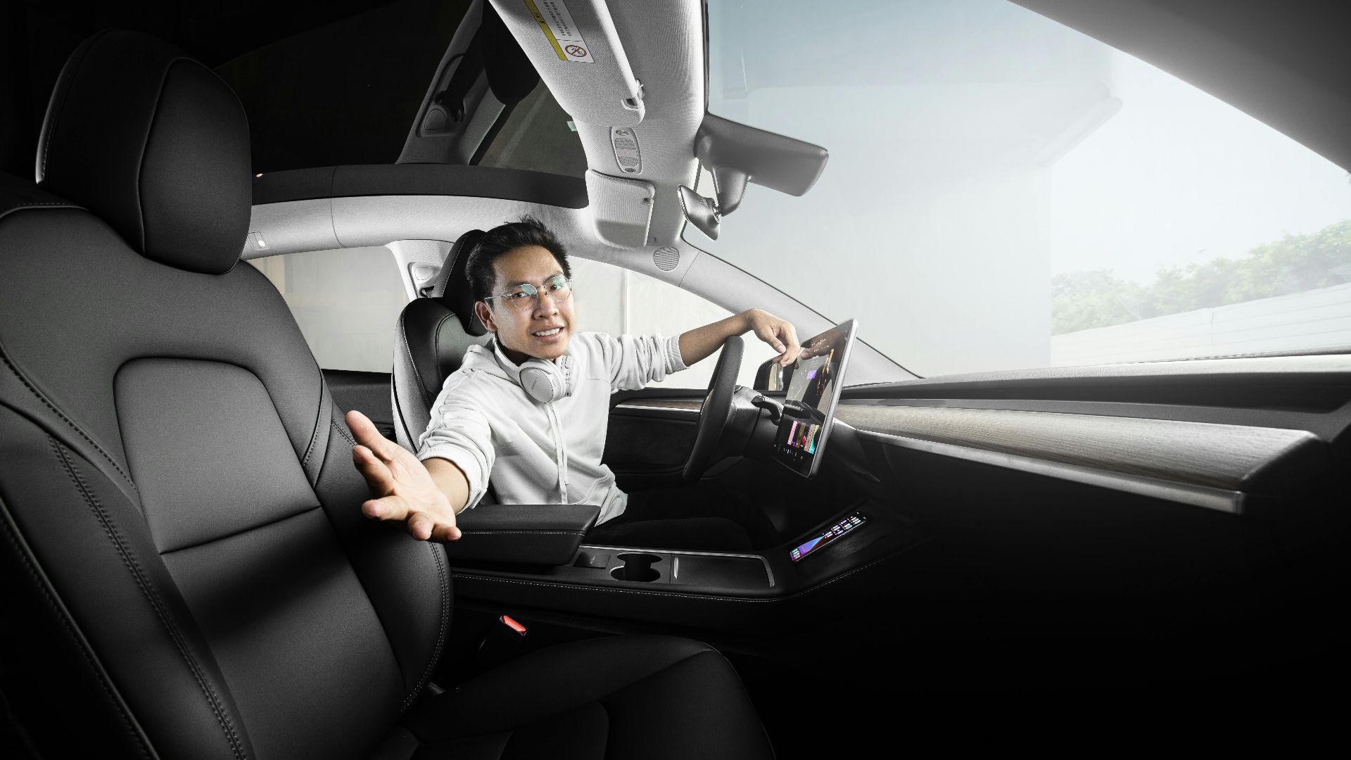 Man extends hand from modern car interior featuring touchscreen technology and sleek design.