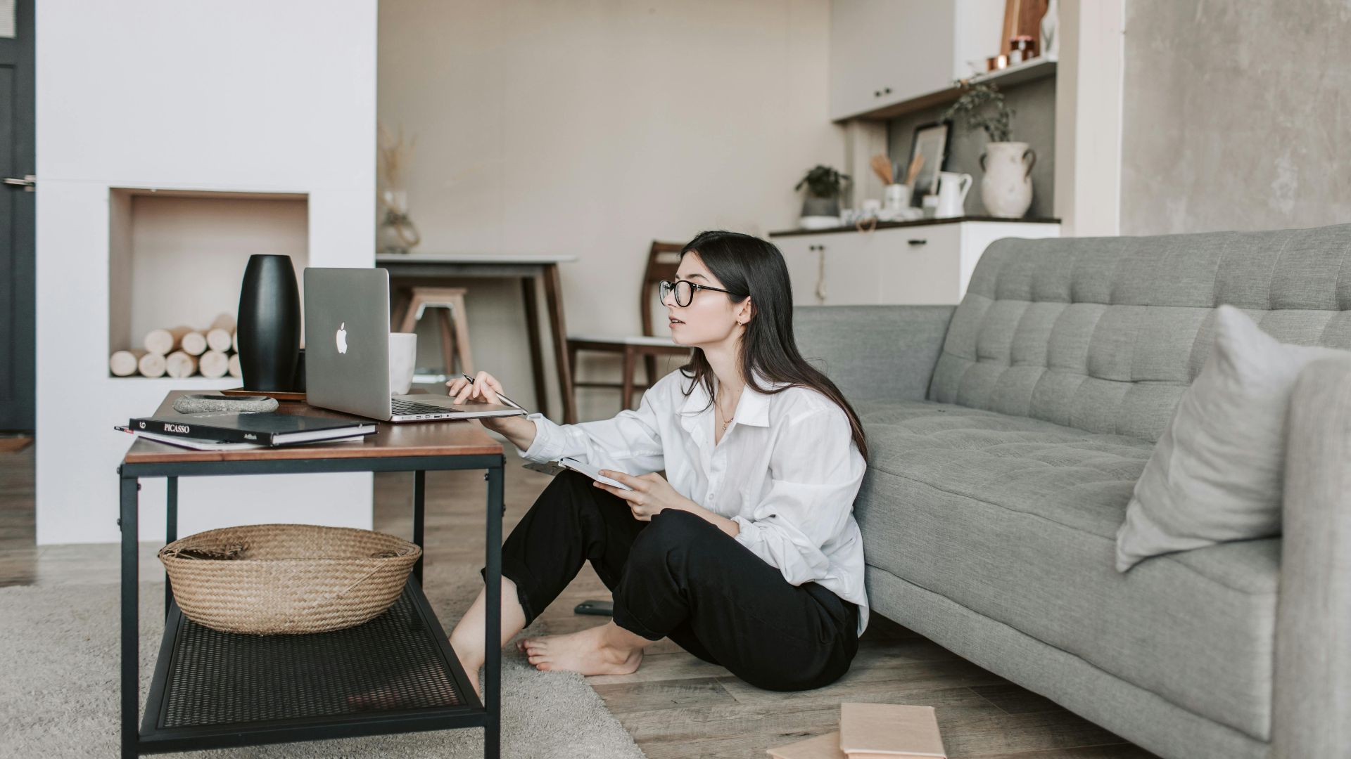 Asian woman working on laptop from cozy living room, showcasing modern home office setup.