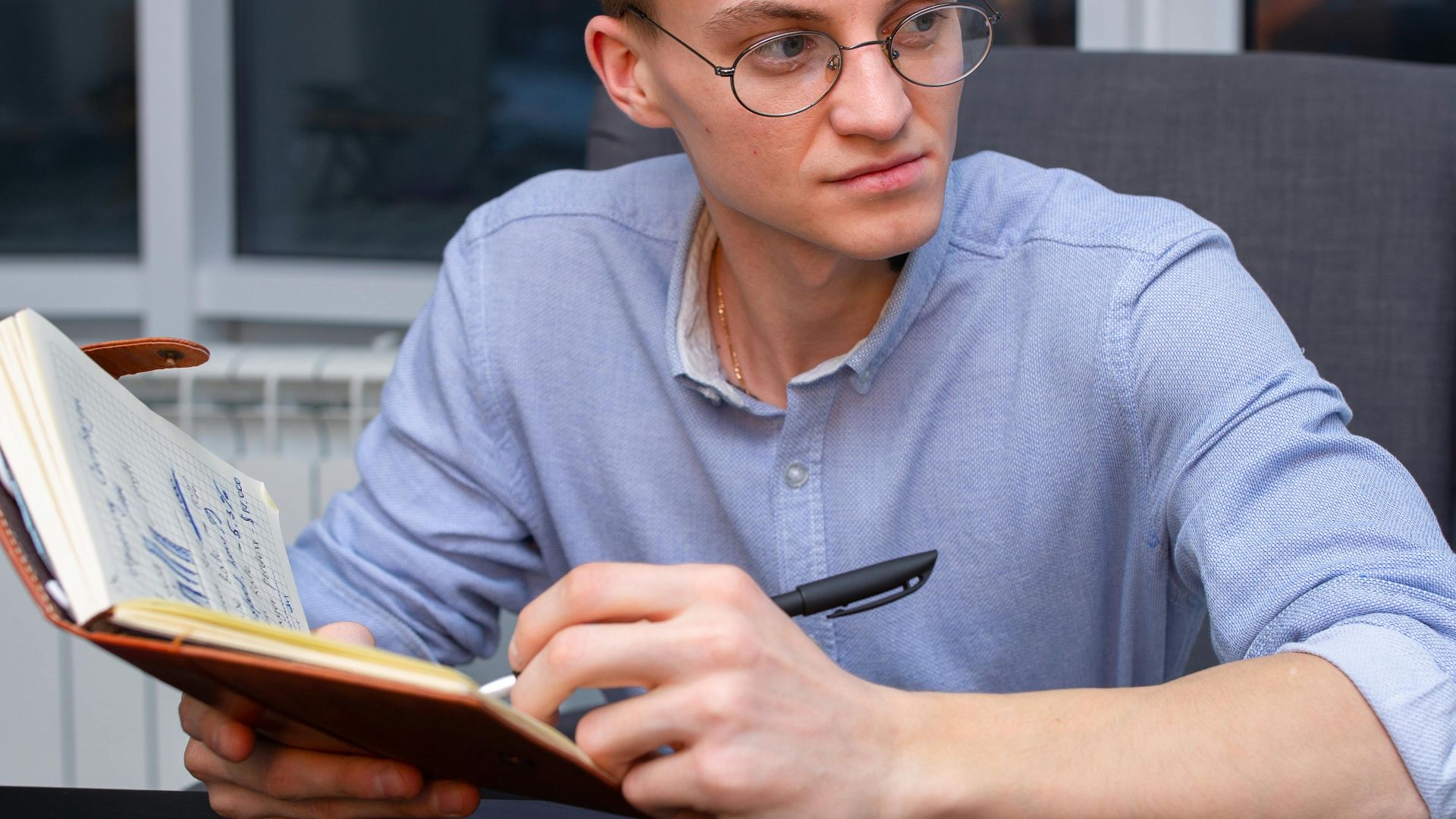 Professional man with eyeglasses and notebook sitting at an office desk, writing notes.