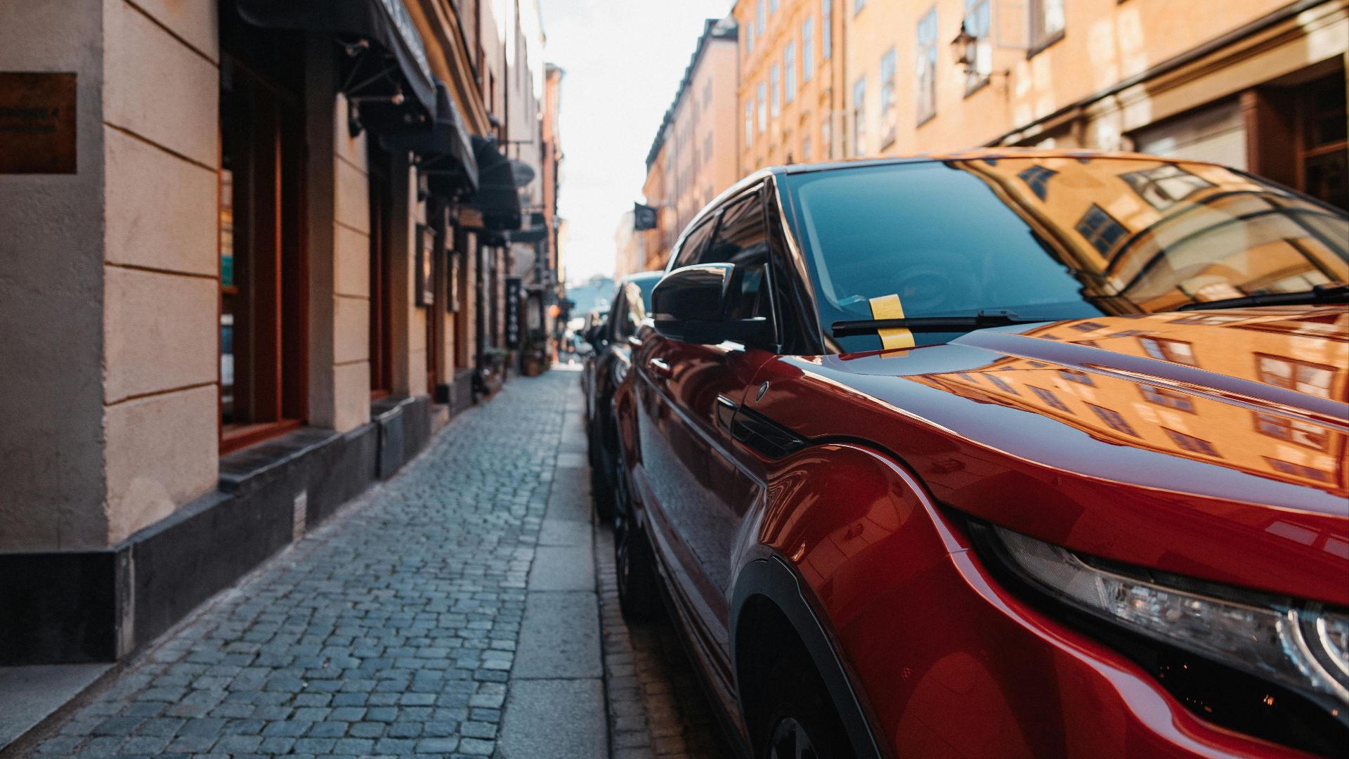 A bright red car parked on a cobblestone street lined with buildings and soft light.