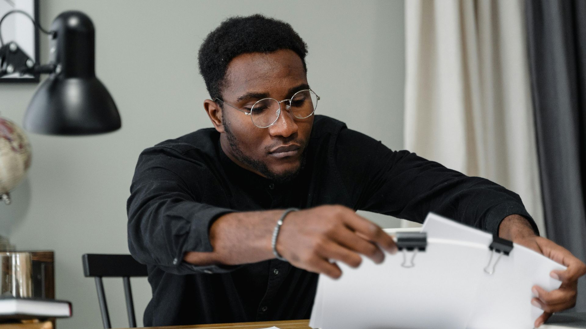 Professional man with glasses reviews documents at a desk in an office setting, emphasizing concentration.