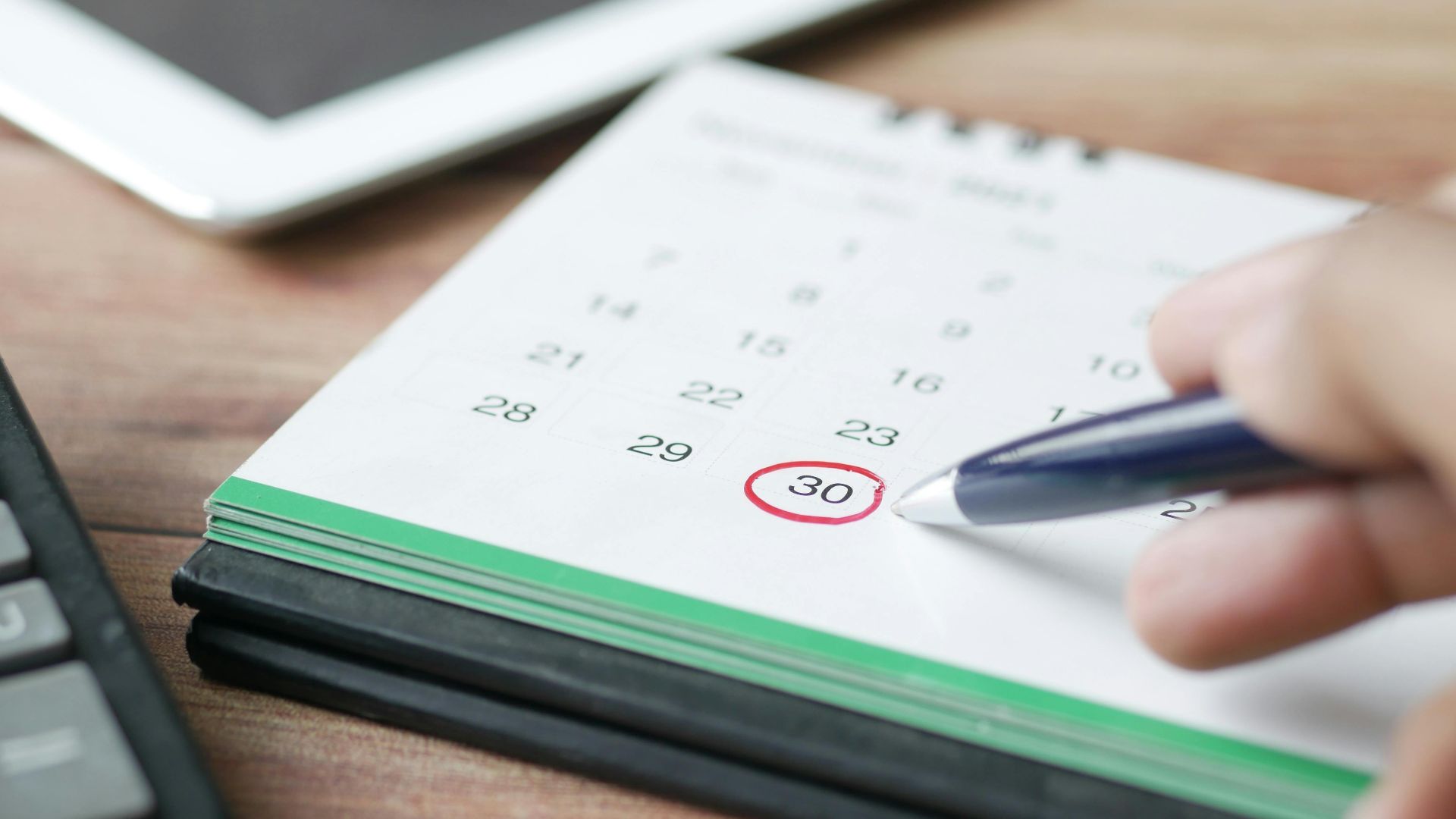 Close-up shot of a hand marking a date on a calendar with a pen, emphasizing planning and scheduling.