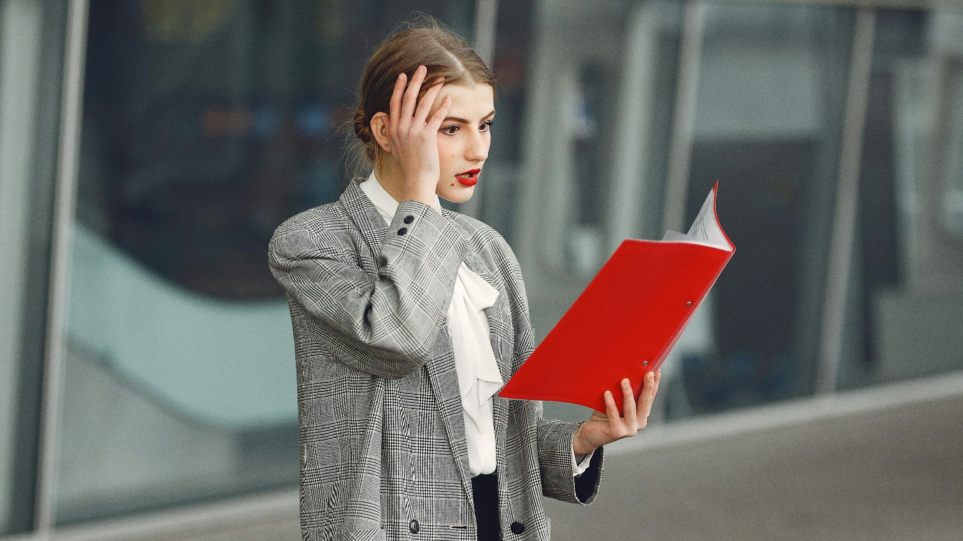 Woman in business attire looking stressed while holding and reading documents outside.