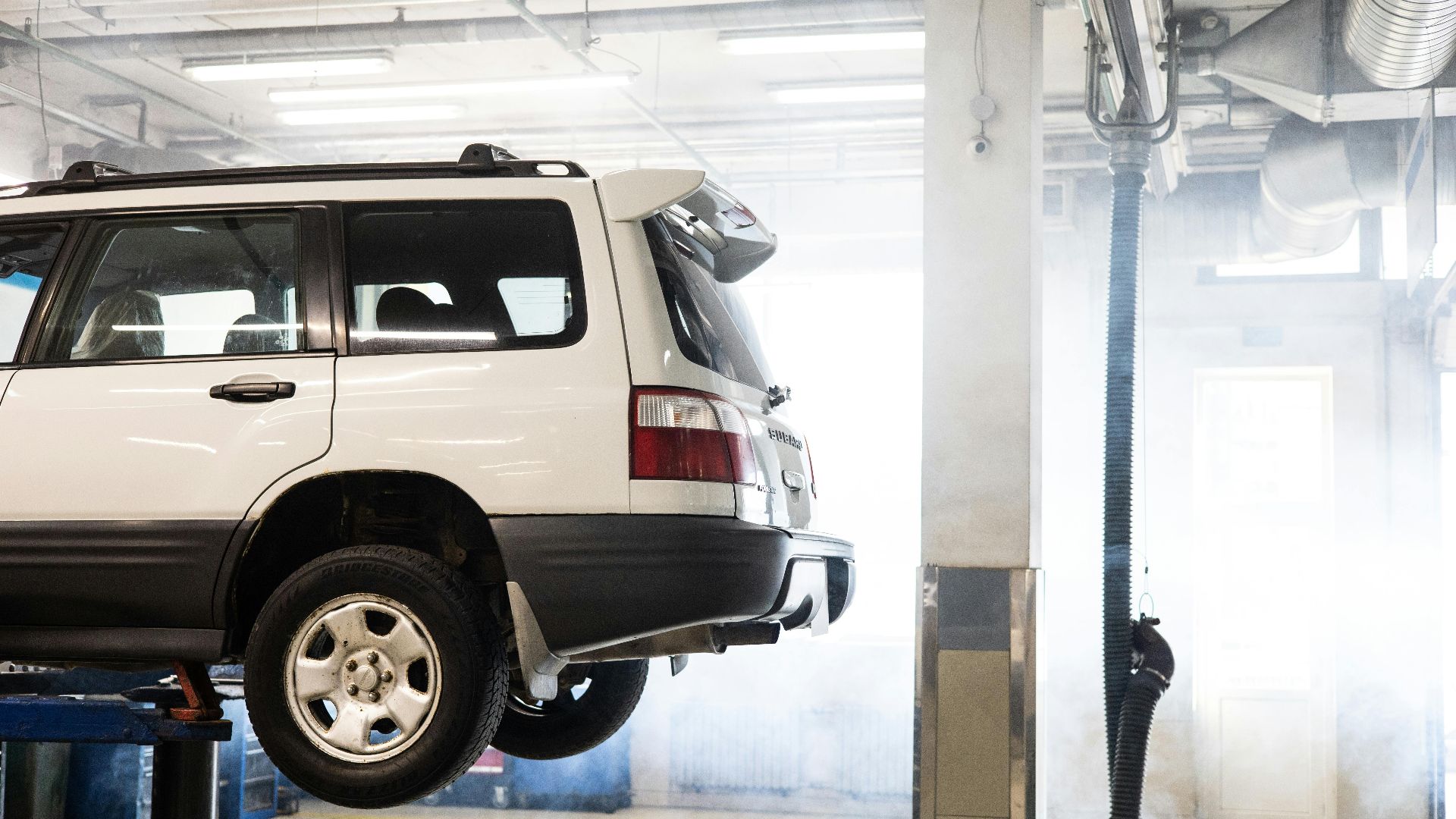 A white SUV is elevated on a lift inside an auto repair shop for maintenance.