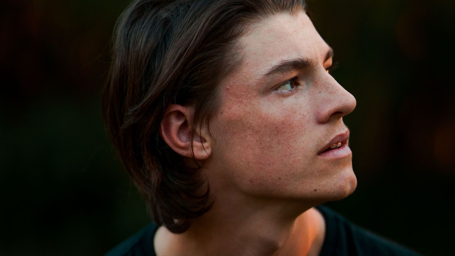A thoughtful young man gazes into the distance against a natural backdrop.