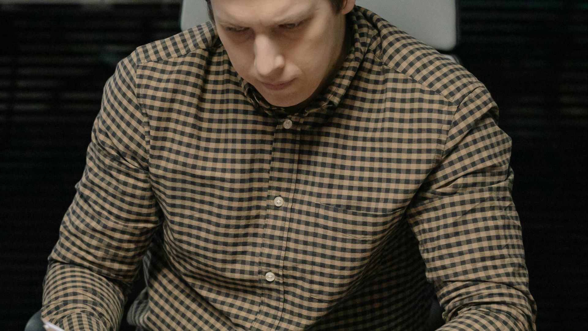 Young man attentively reading documents in an office setting with a formal demeanor.