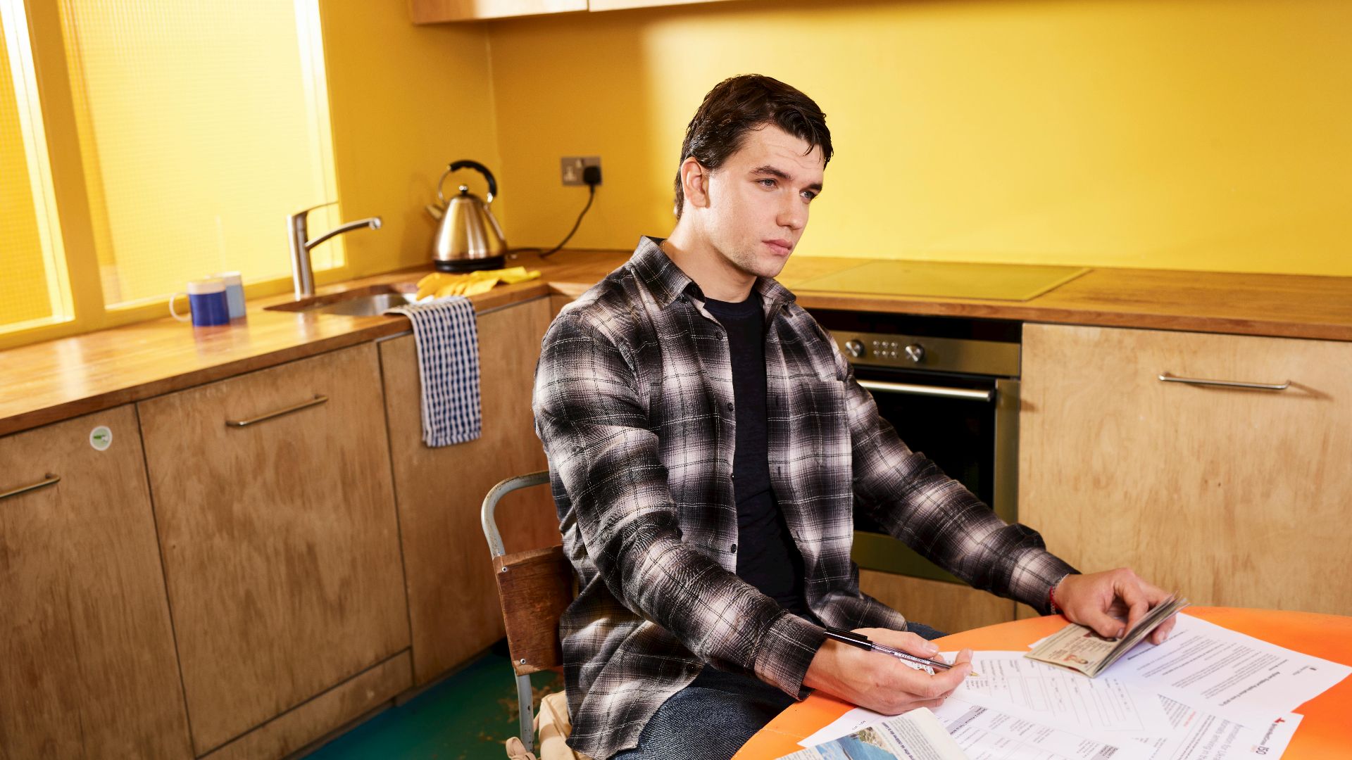 Man sitting in kitchen reviewing bills and a check with smartphone nearby.