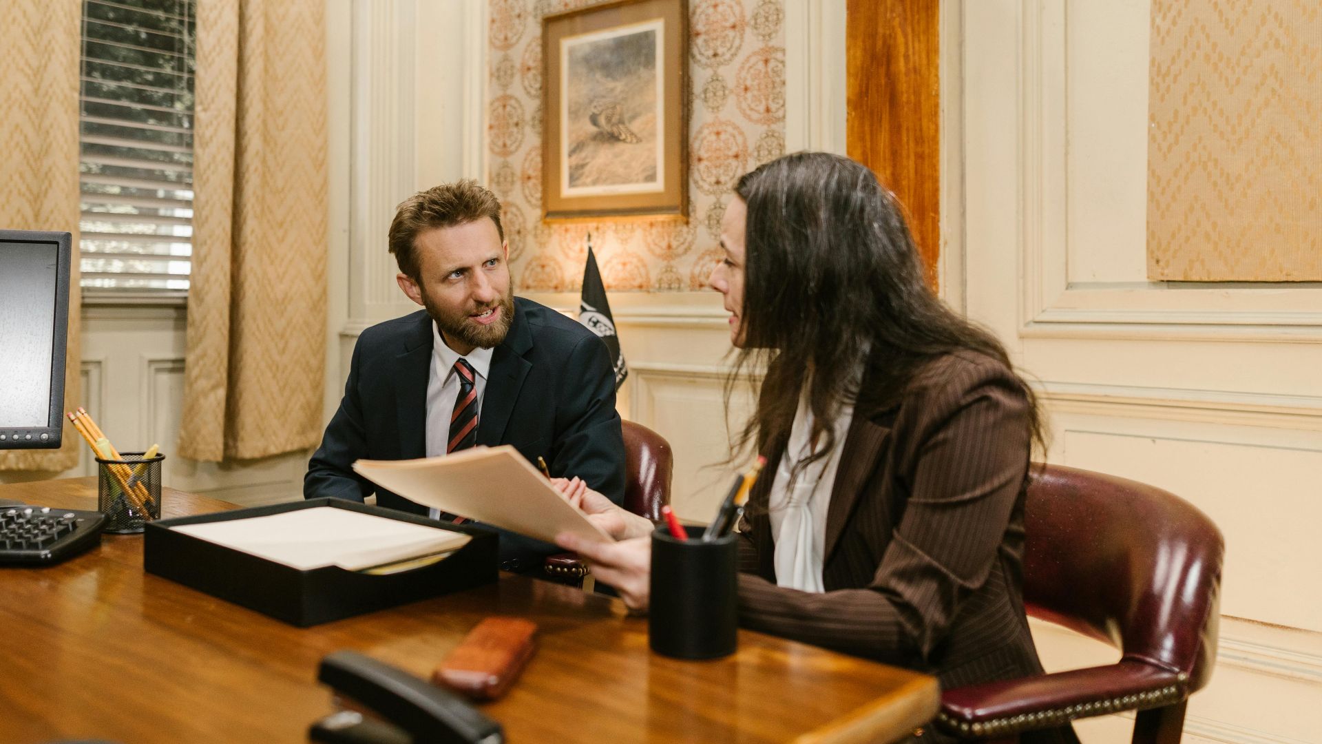 Two professionals engaged in a business discussion in an office setting, reviewing legal documents.