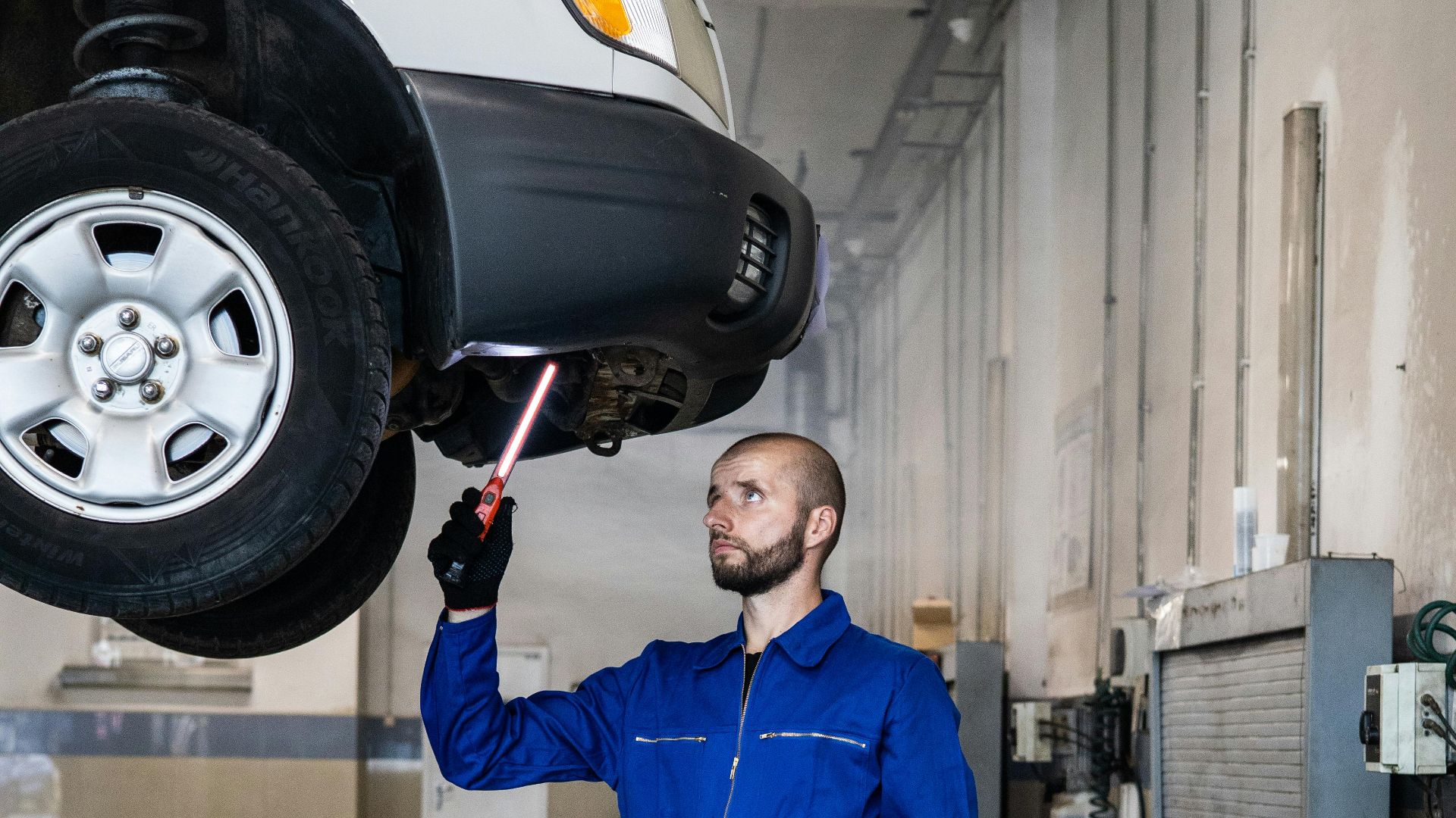 Mechanic in blue coverall inspecting car in auto repair shop. Professional vehicle maintenance in progress.