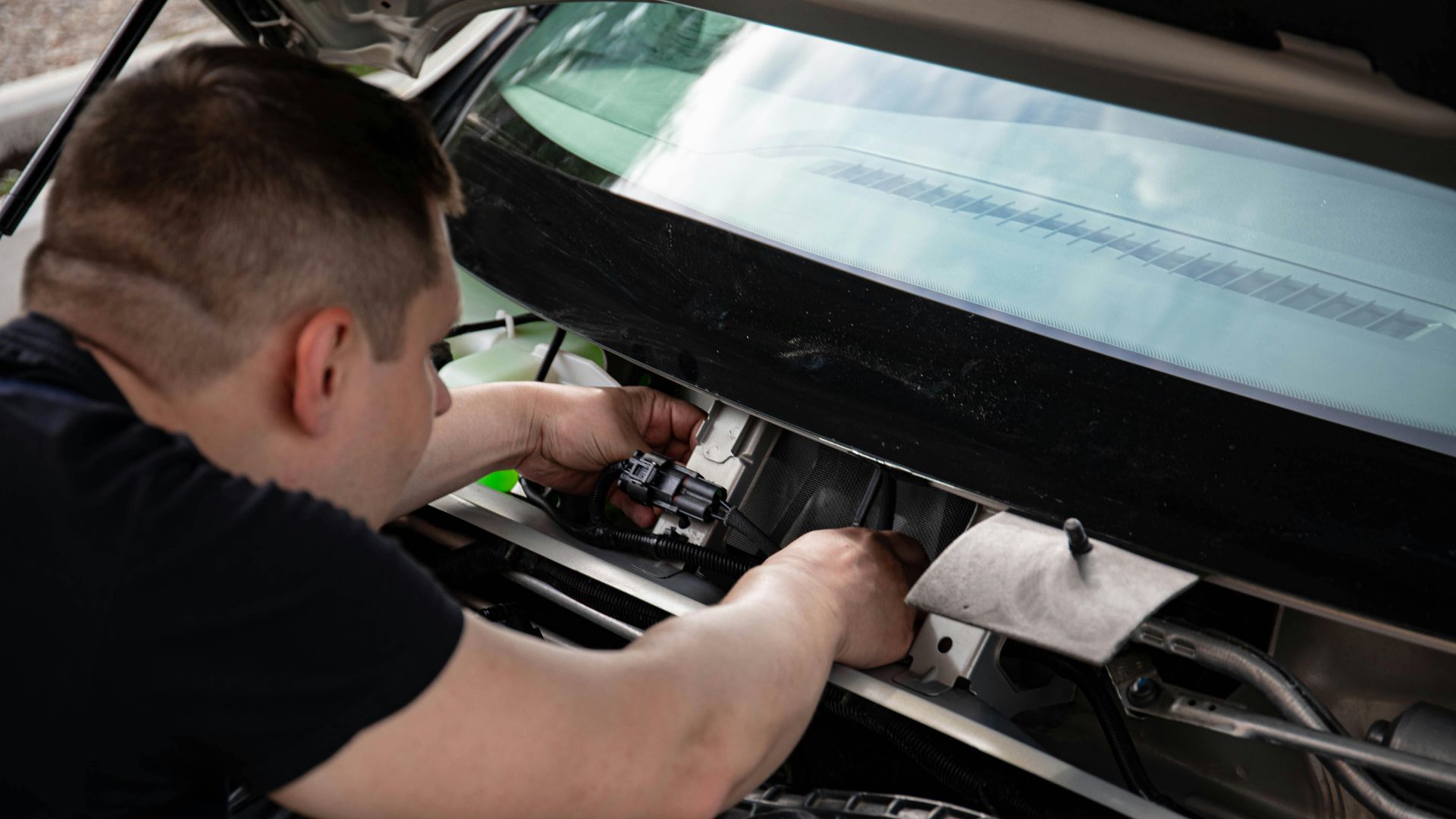 A mechanic working on car engine repairs inside a workshop setting.