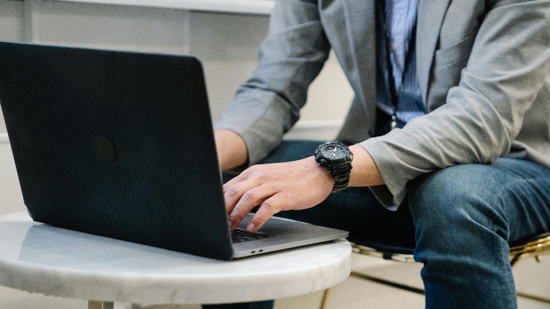 A focused man typing on a laptop in a modern office environment, showcasing casual work attire.