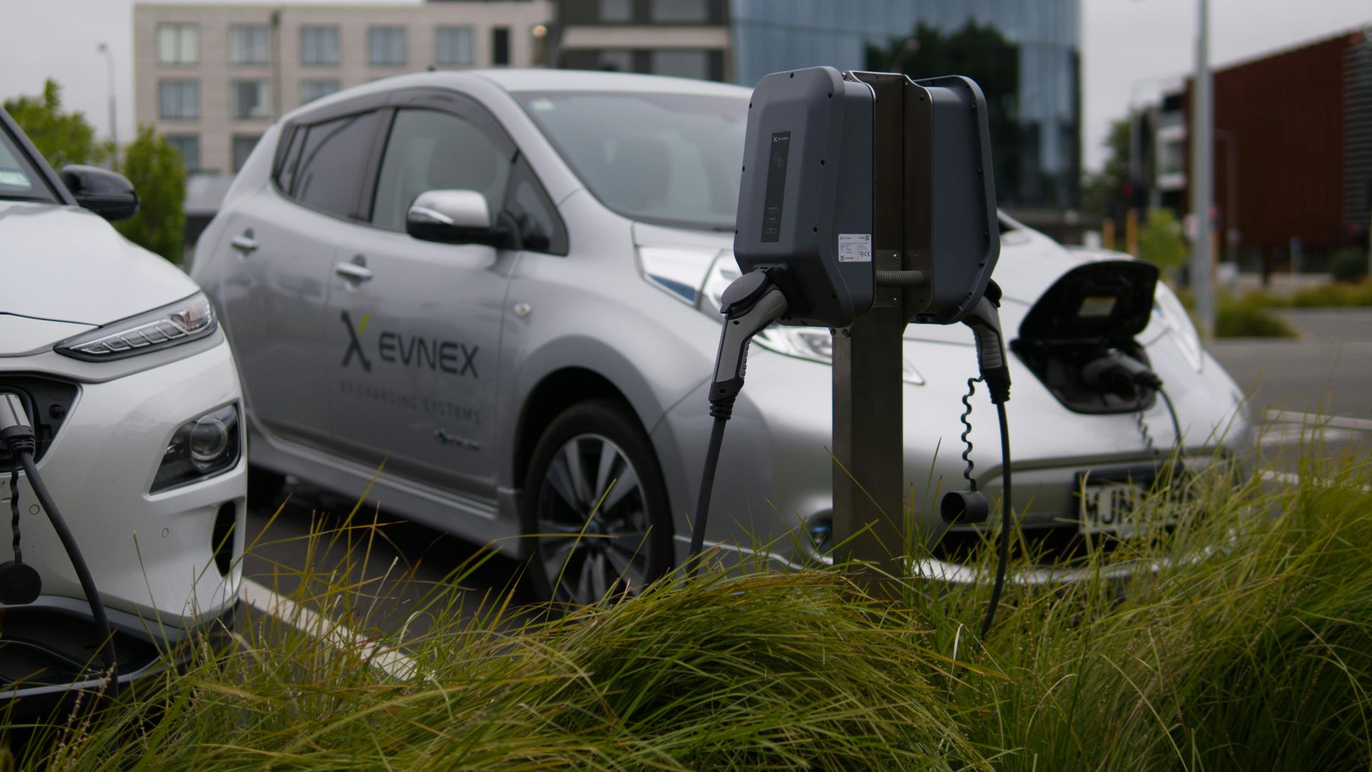 Electric vehicles at a charging station in Christchurch parking lot with modern architecture.