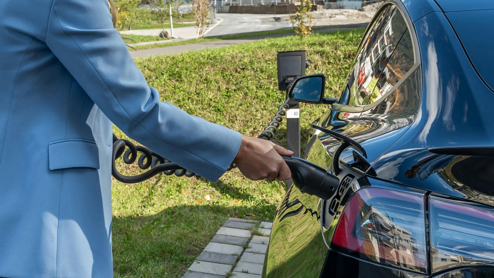 Person connecting an electric car to a charging station outdoors, showcasing green energy transition.