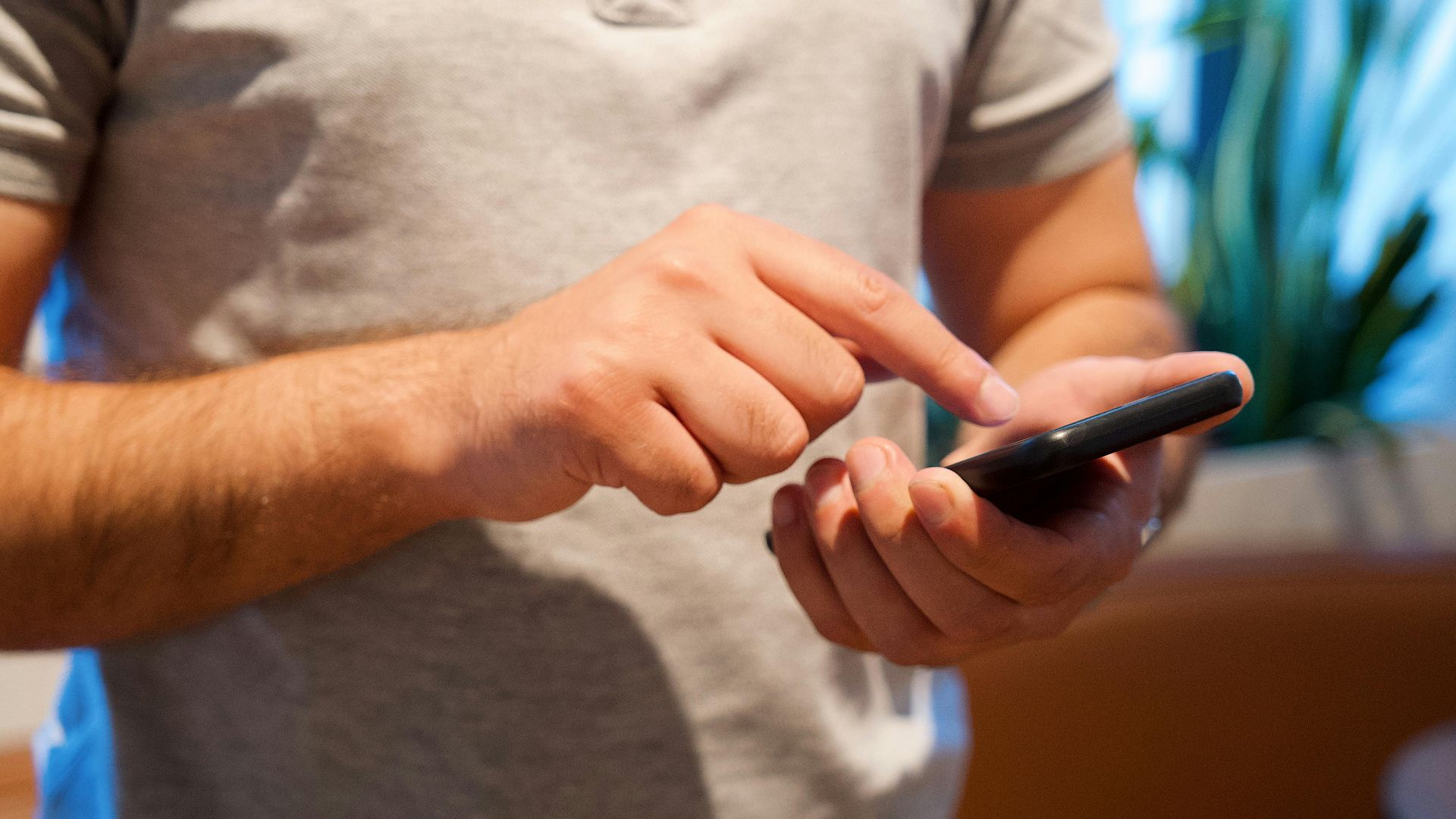 Adult male using smartphone in a bright indoor setting, focusing on the device and interaction.
