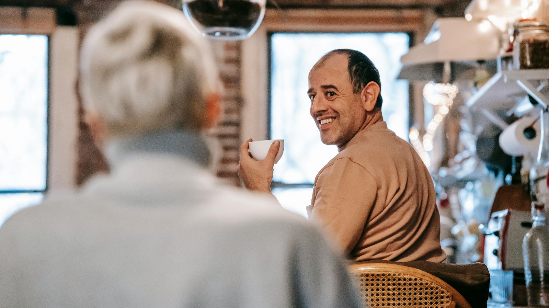 Back view of unrecognizable female in casual clothes speaking with happy middle aged ethnic husband drinking coffee at home