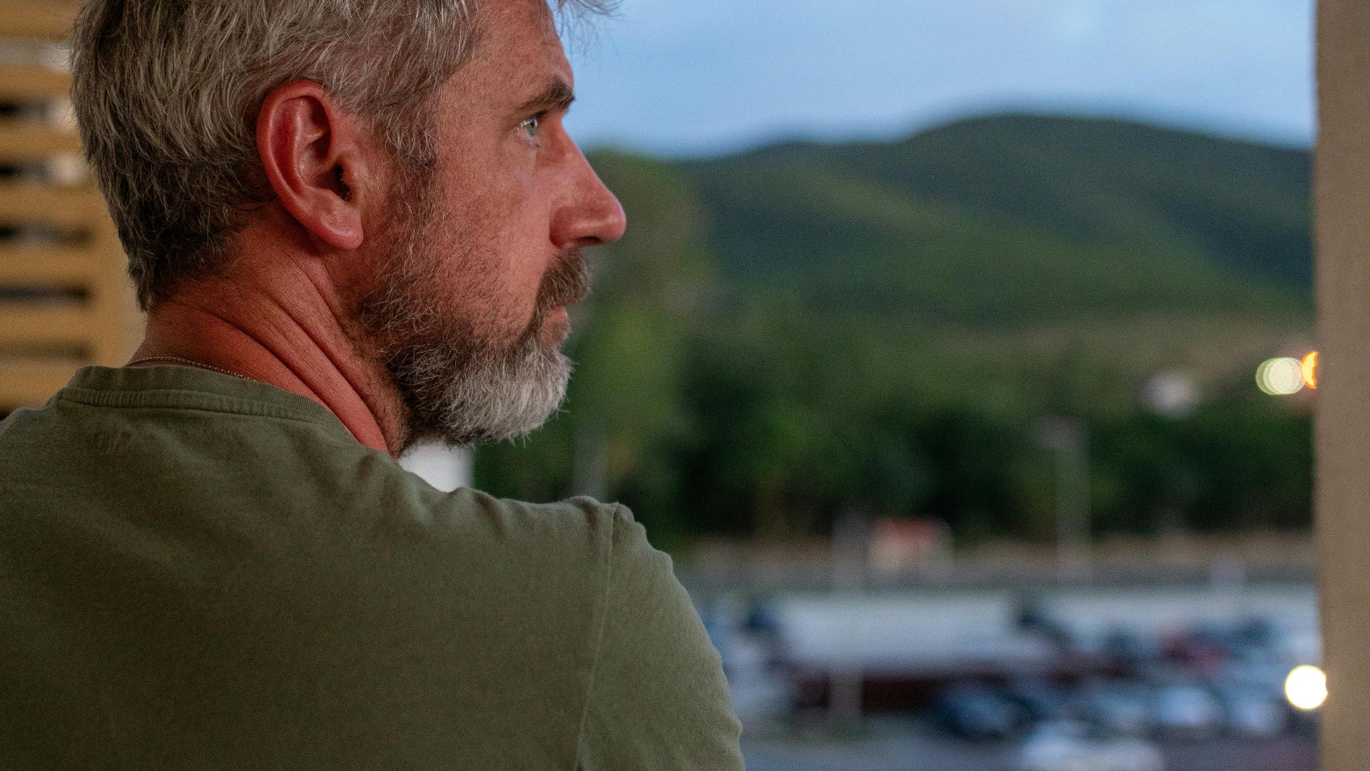 Adult man on a balcony enjoying a peaceful outdoor view at twilight.