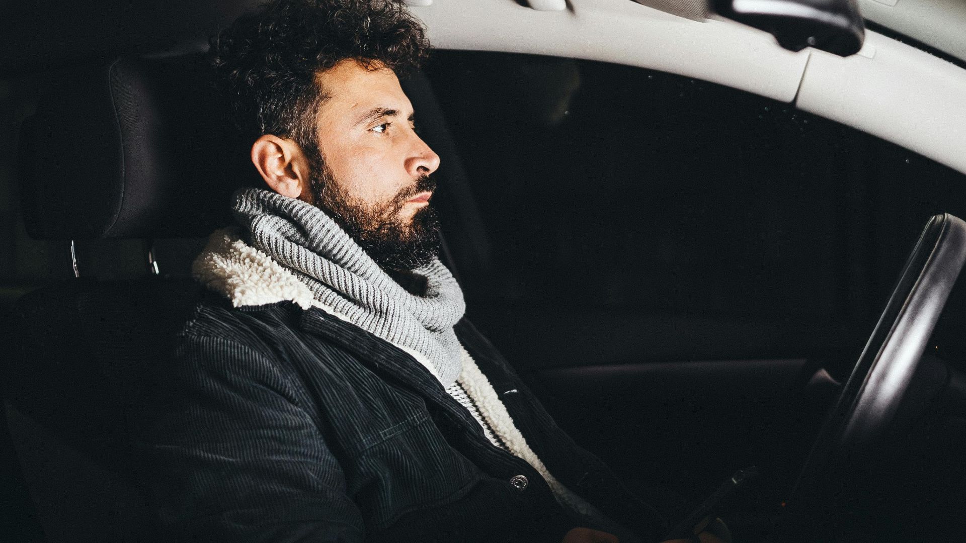Adult man driving a car at night, illuminated and using a smartphone.