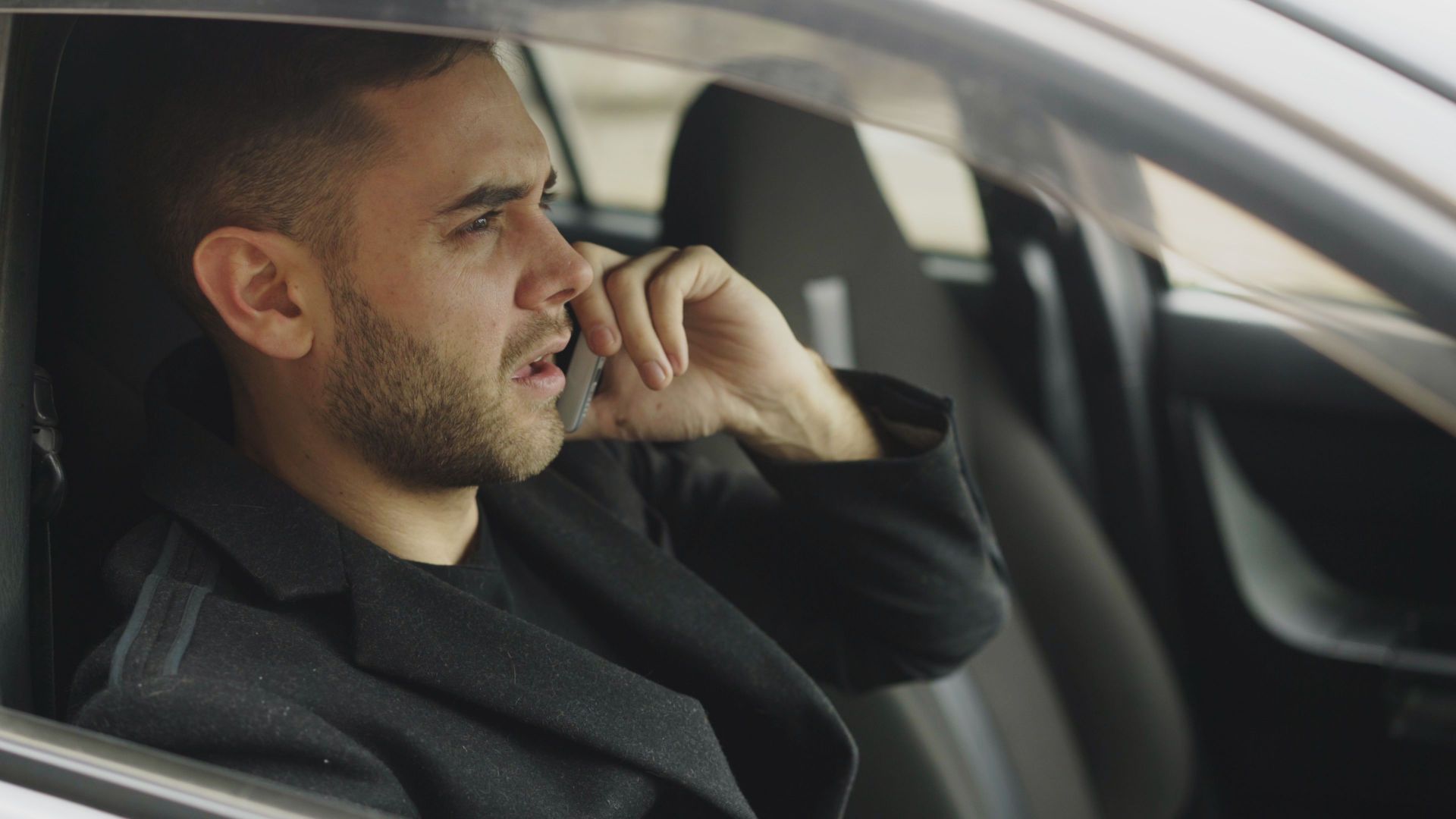 Man in car talking on smartphone, appearing thoughtful.