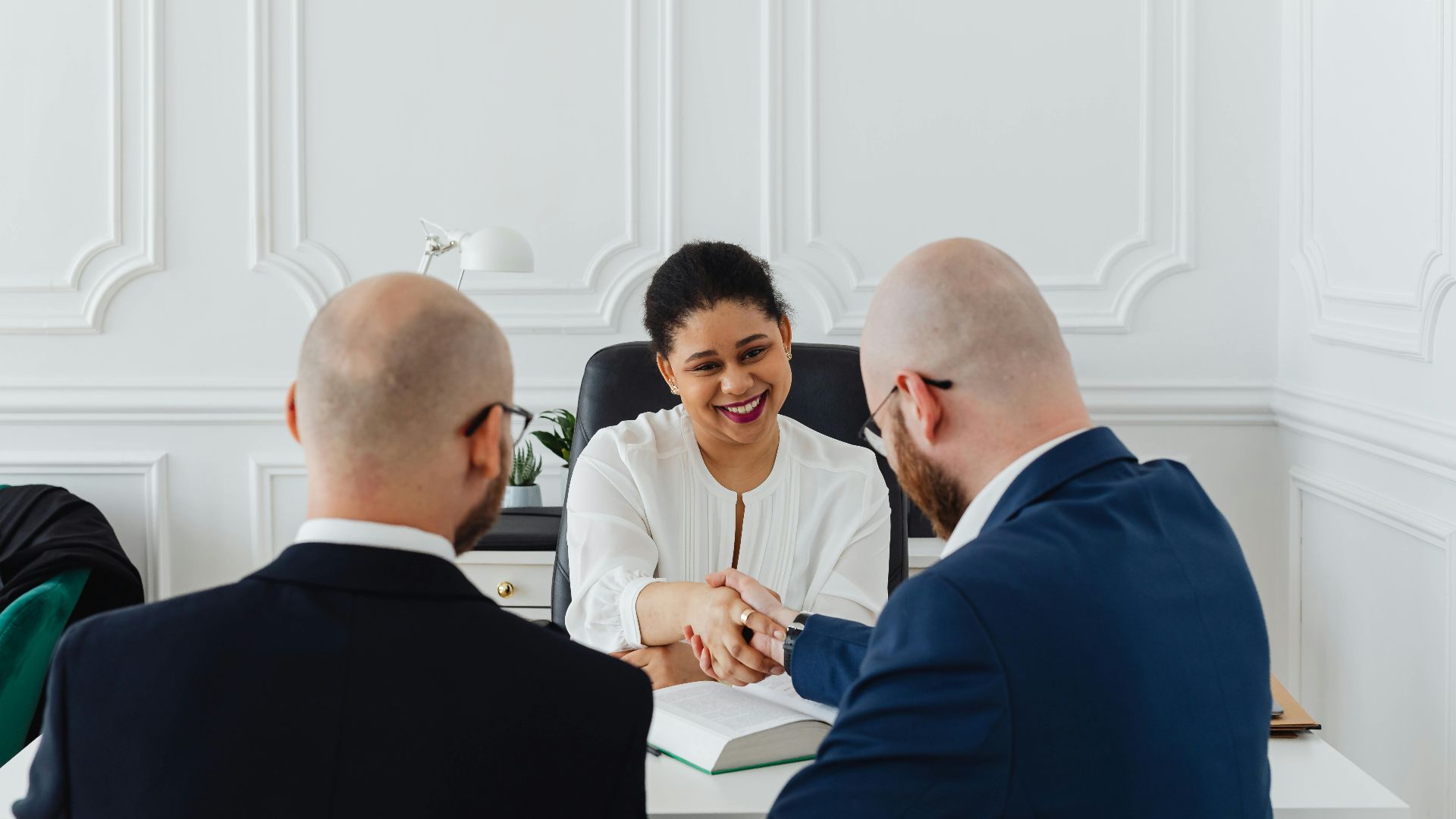 Diverse professionals in a business meeting, shaking hands across a table, indoors.