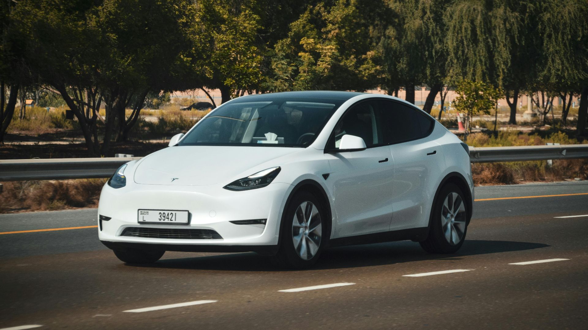 A sleek white electric car cruising on a sunny highway in Abu Dhabi, UAE.
