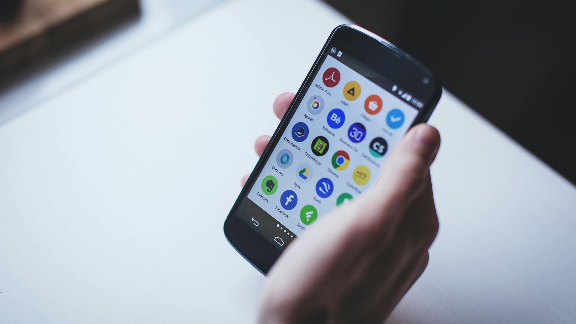 Close-up of a person holding a smartphone with various app icons visible on the screen.
