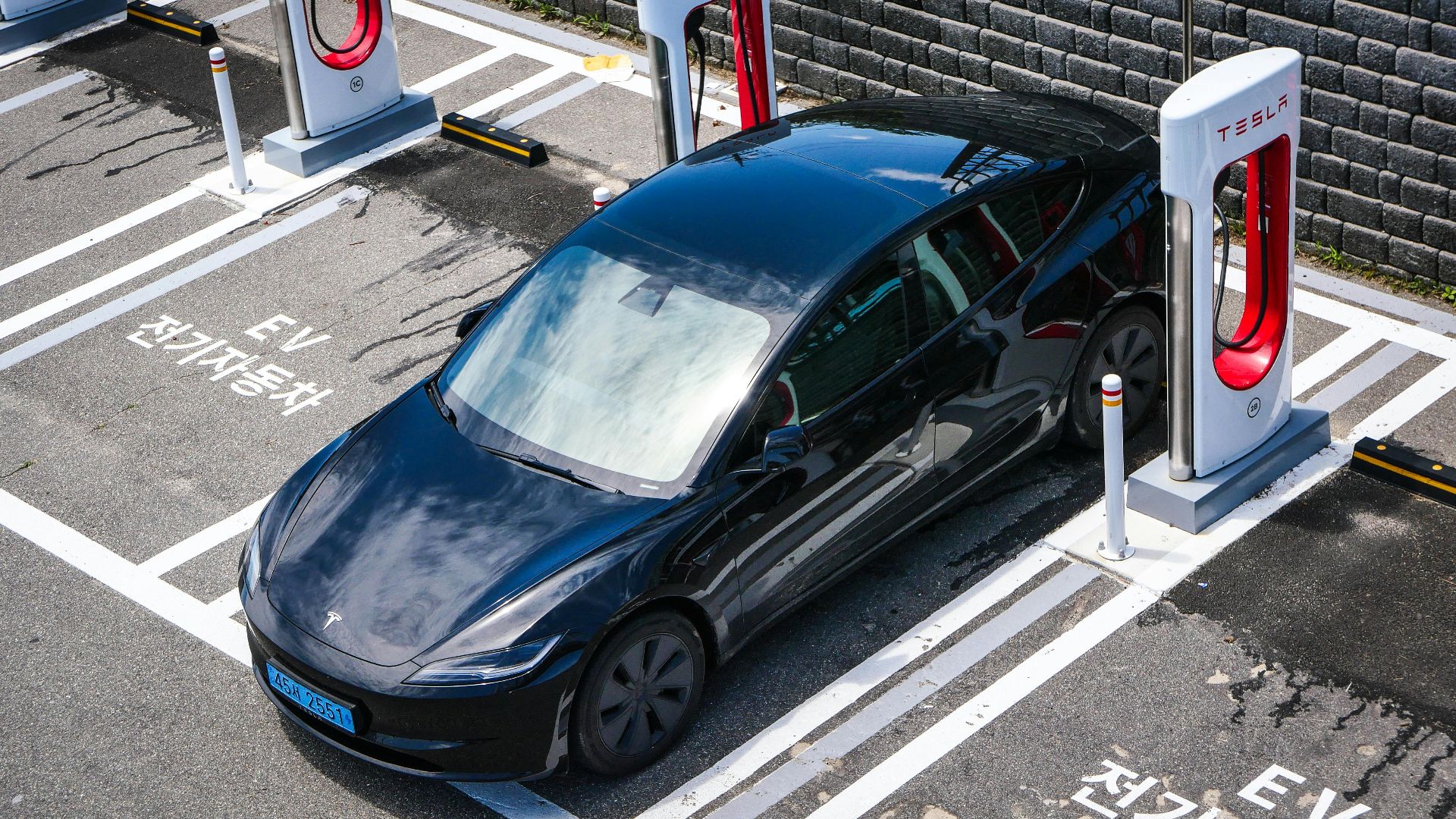 A black Tesla parked at a charging station in an urban setting.