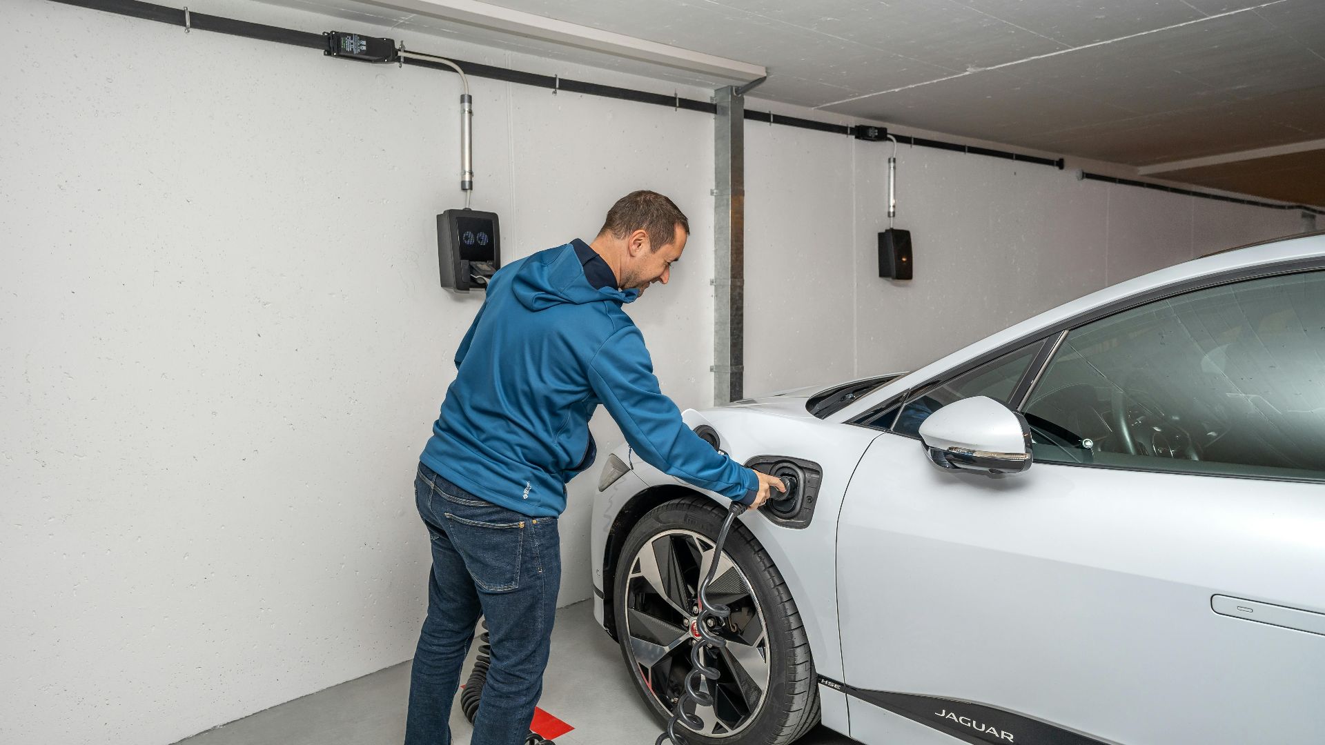 A man connects an electric car to a charging station in a modern indoor garage setting.