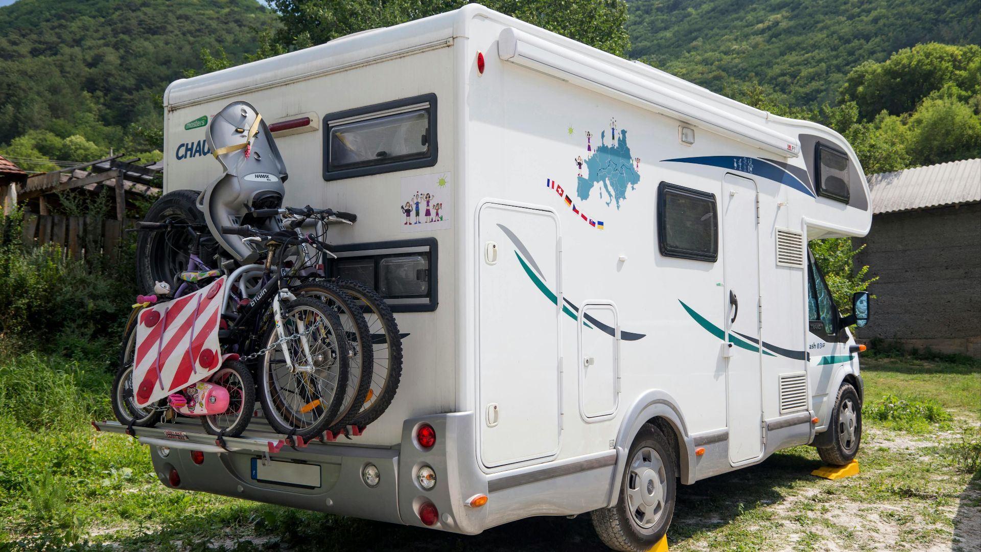 An RV with bicycles attached in a scenic outdoor setting, surrounded by mountains and greenery.