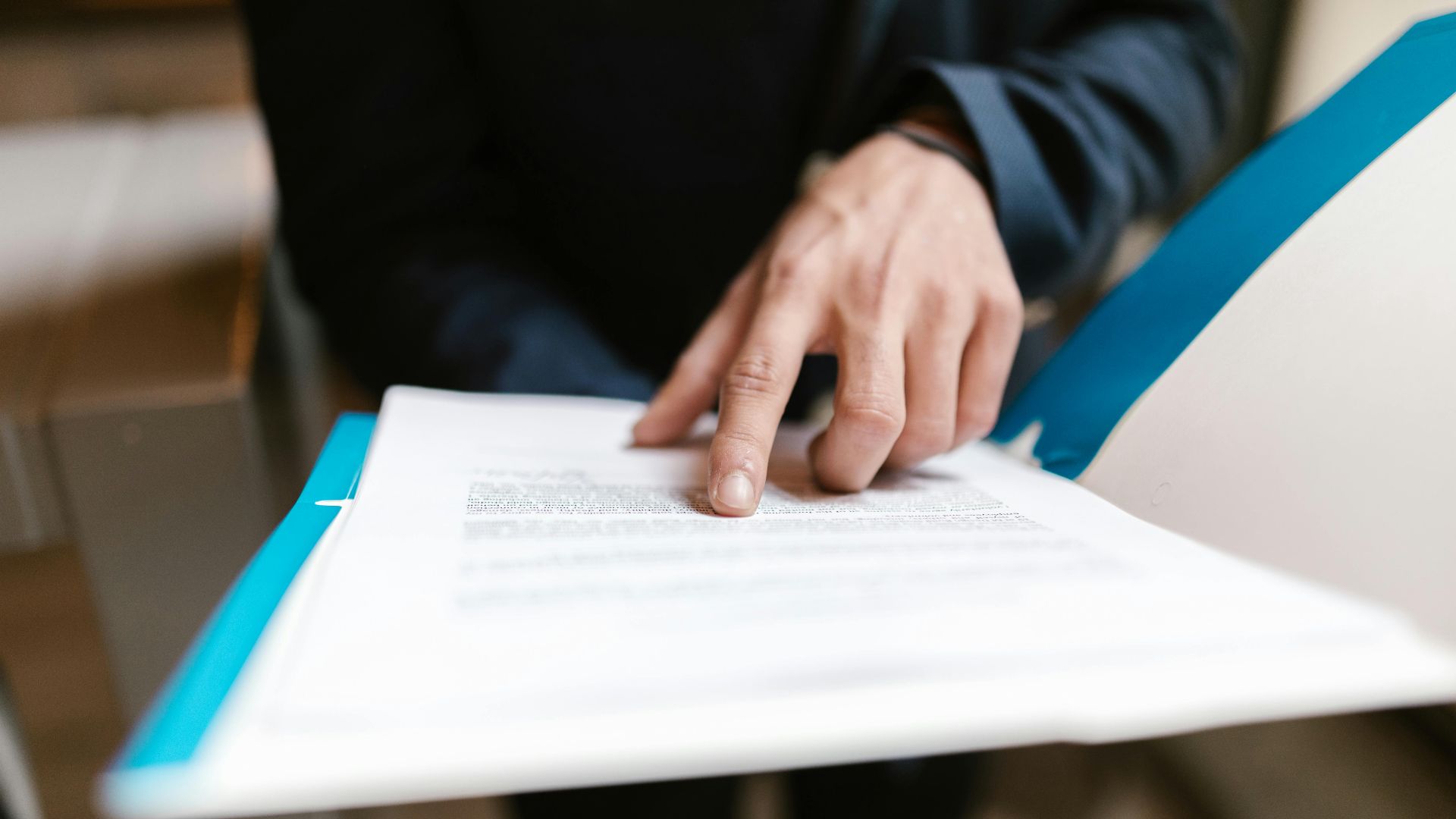 Close-up of a hand pointing at text on a business document in an office environment.
