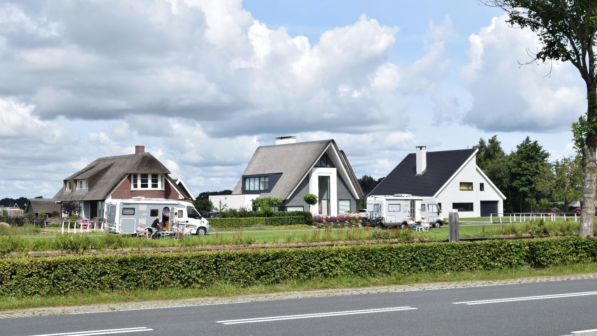 Empty asphalt road with fence and row of country houses under blue sky with clouds