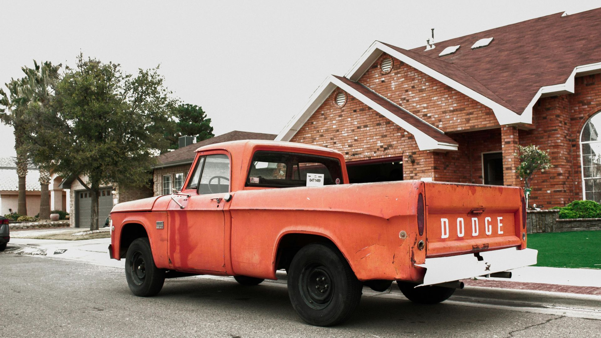 Old red Dodge truck parked in a quiet suburban neighborhood street.