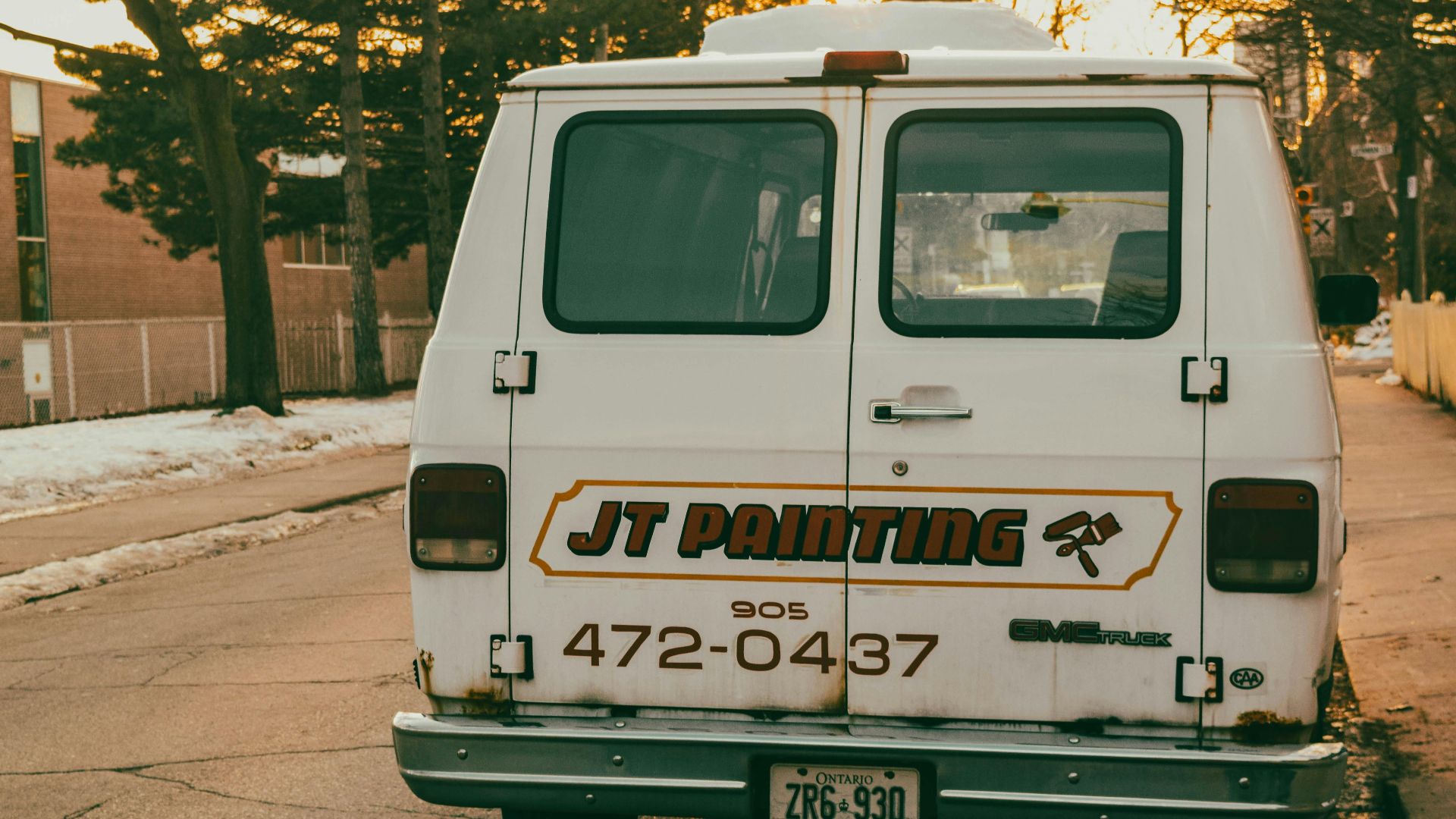 Rear view of a vintage painting service van parked on a snowy street during winter sunset.