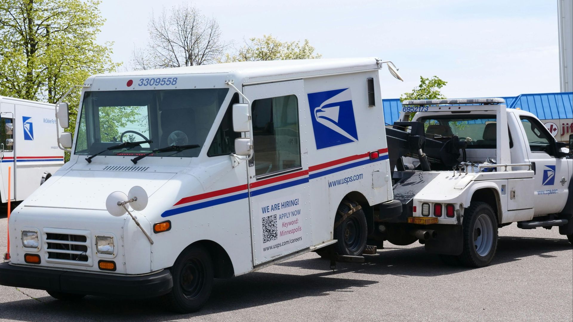 A United States Postal Service (USPS) mail truck is being towed outdoors on a clear day.