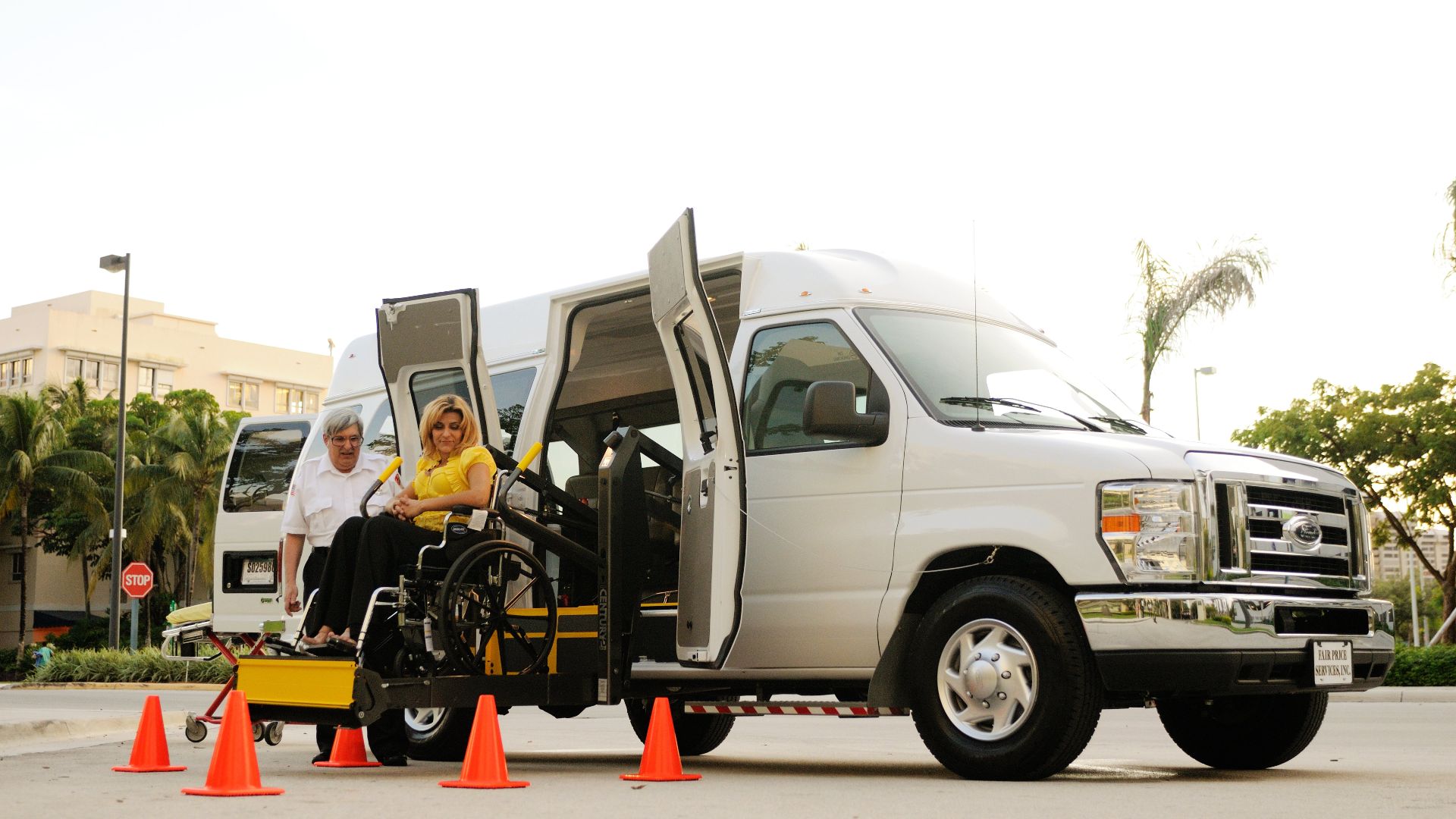 A woman in a wheelchair uses a lift to board an accessibility van assisted by a driver.