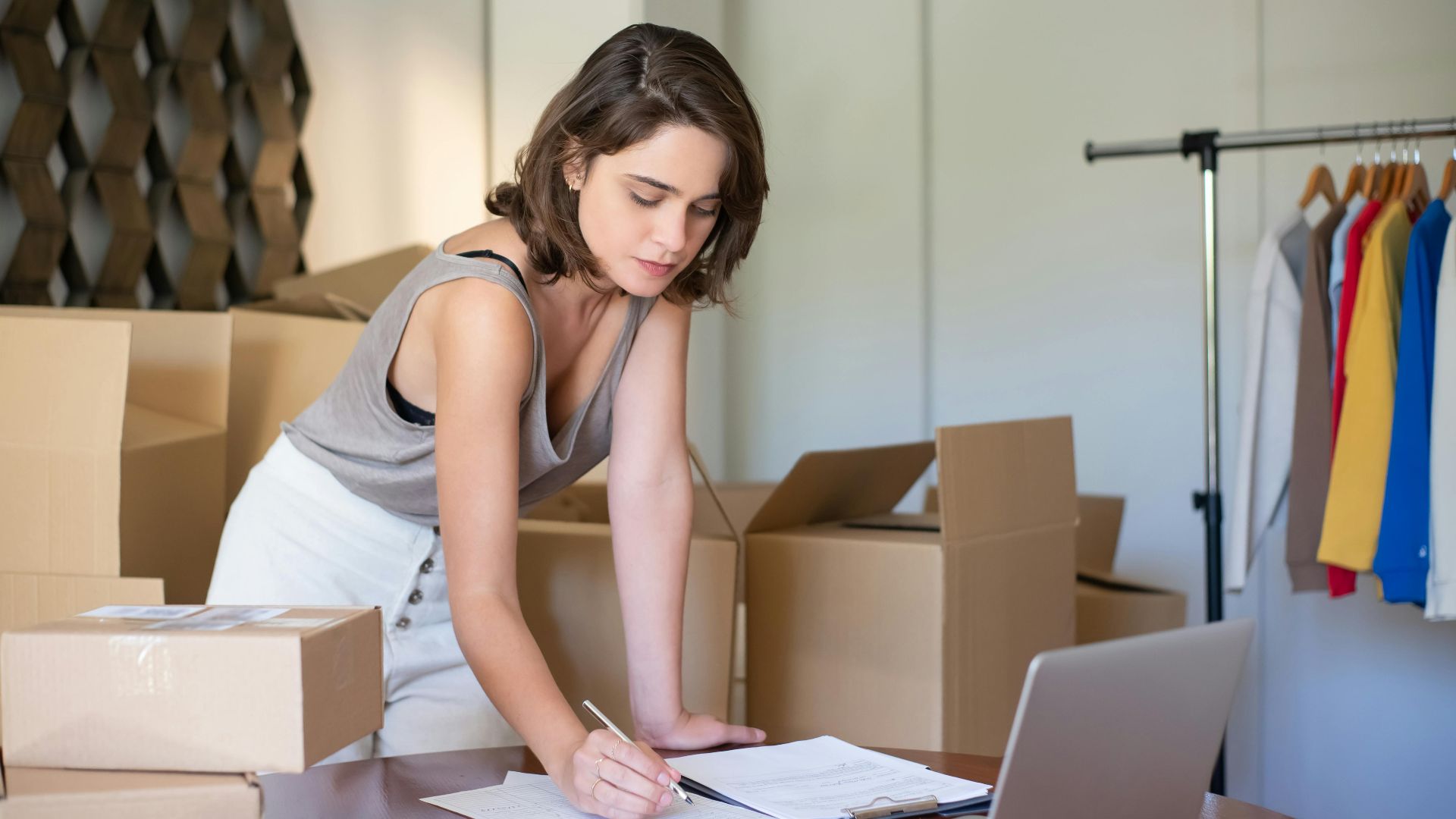 Young woman managing her online clothing business from home office with boxes and laptop.