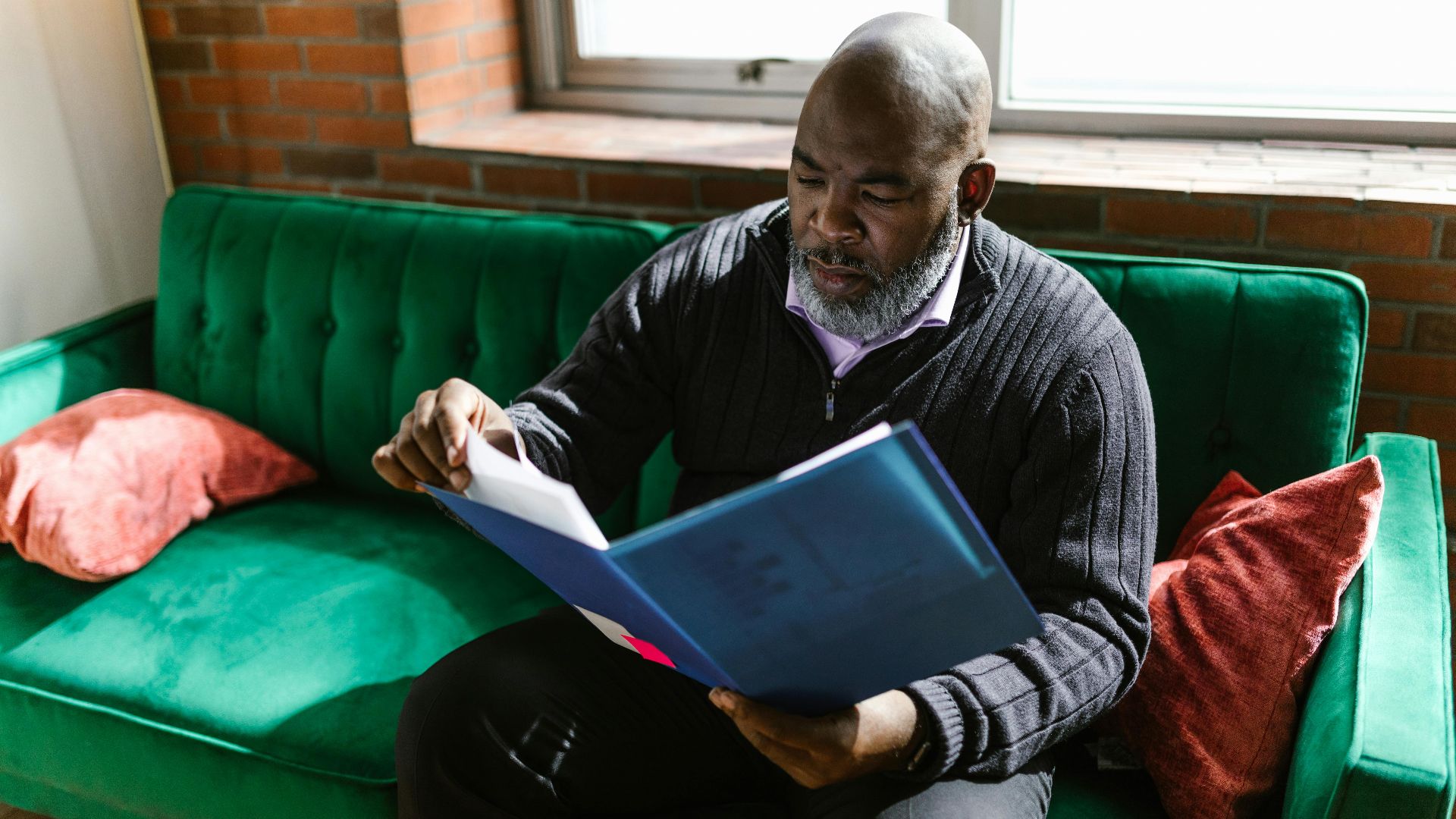African American adult man reviewing documents on a green sofa, indoors.