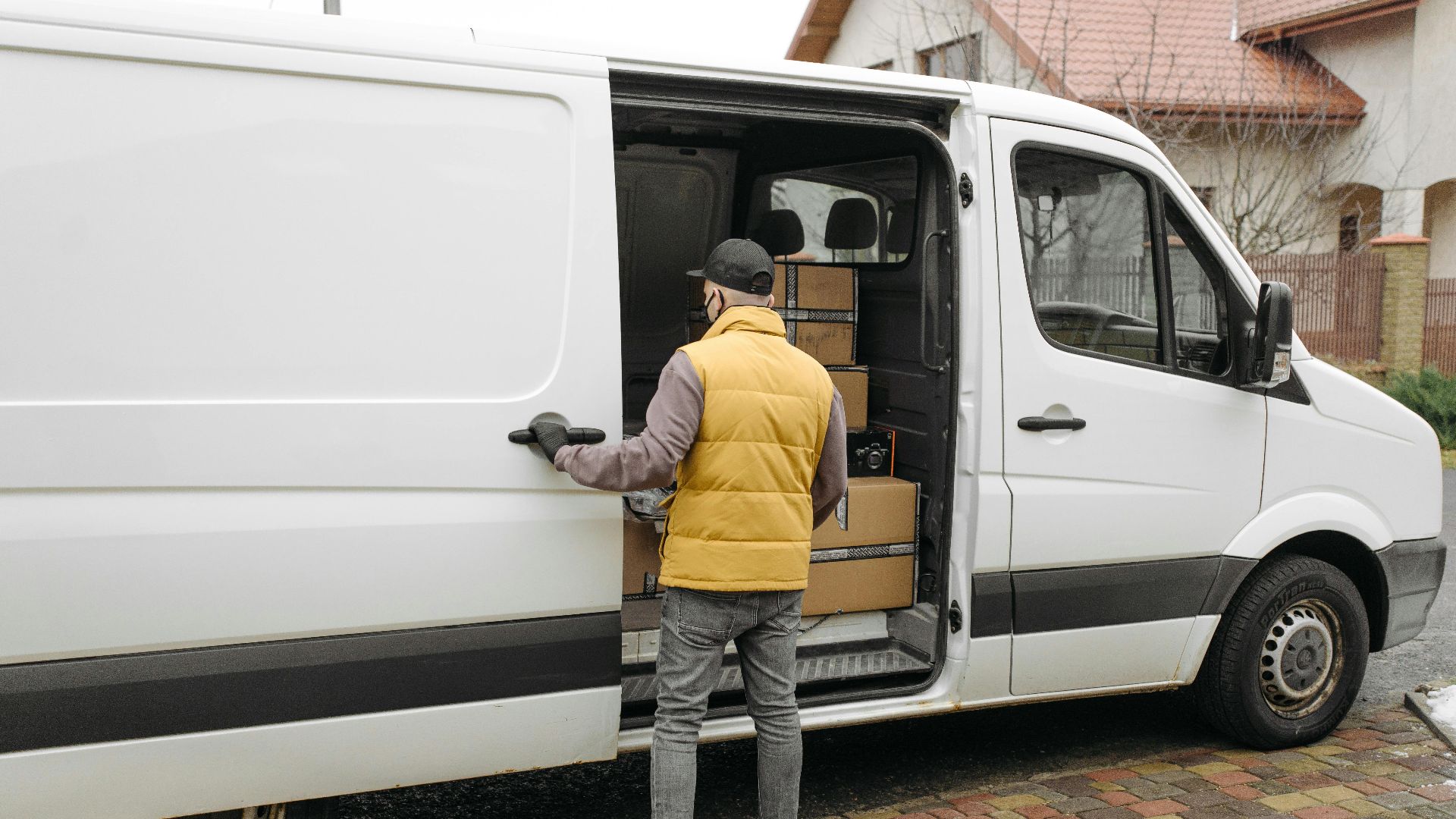 A delivery driver loads packages into a white van on a residential street.