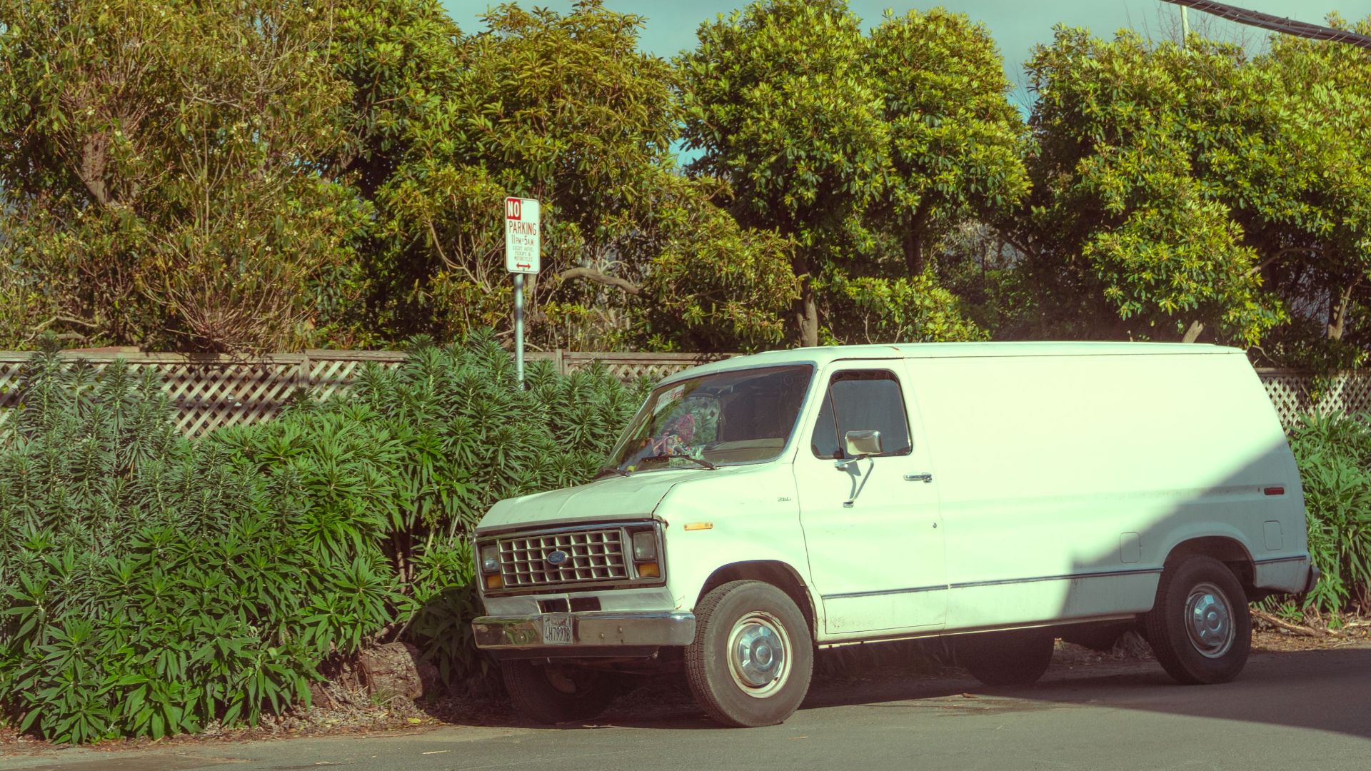 A classic white van parked on a sunny suburban street with clear blue skies.