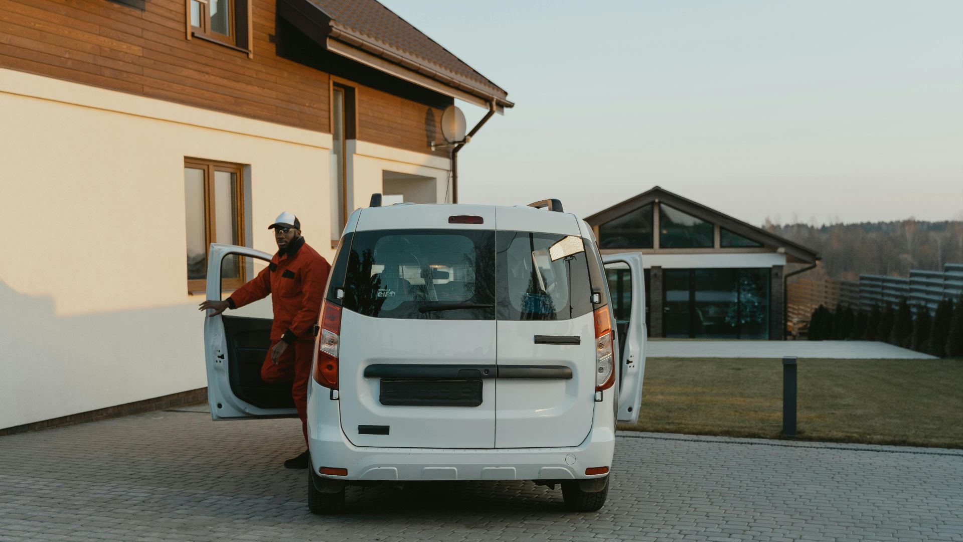 A worker in uniform exits a white van parked in a residential driveway during daytime.