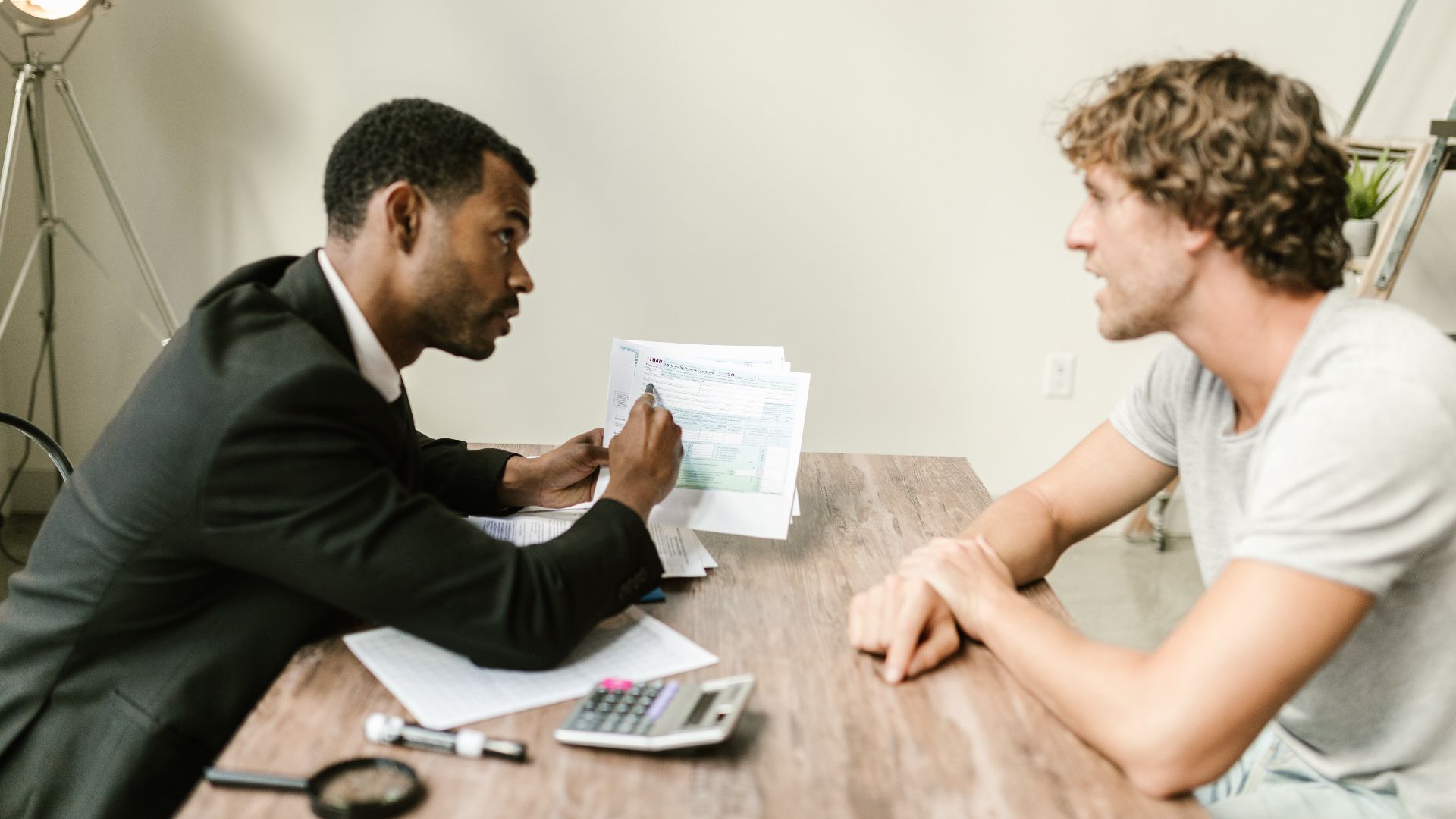 A financial advisor discusses paperwork with a client at a desk in a modern office.