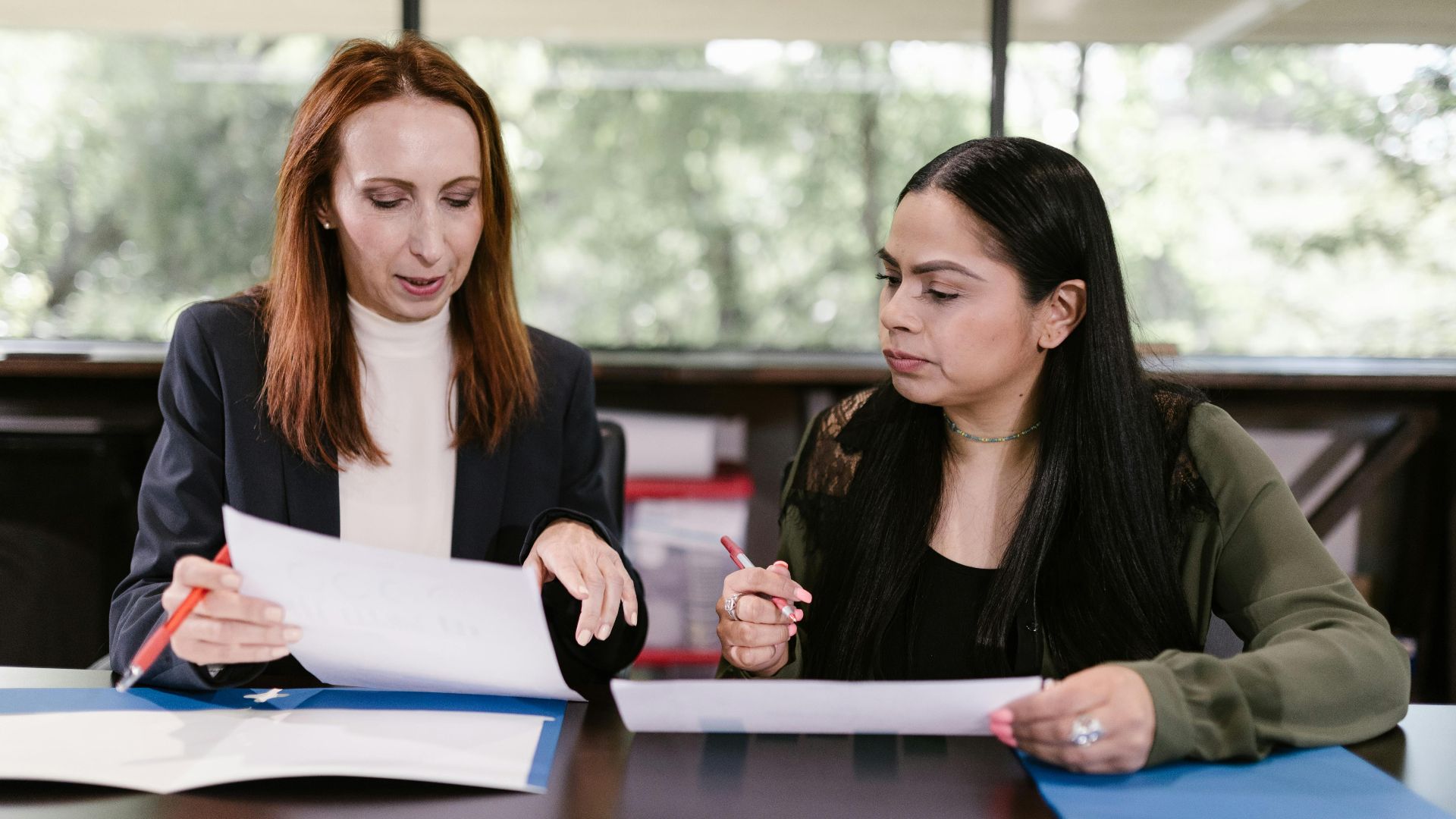 Two professional women reviewing documents in a well-lit office setting.