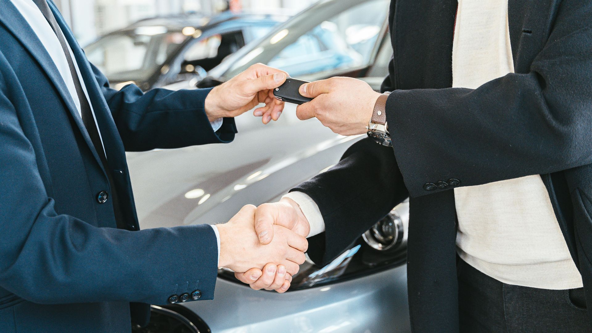 Two businessmen shaking hands and exchanging car keys in a dealership. Symbolizes a successful deal.