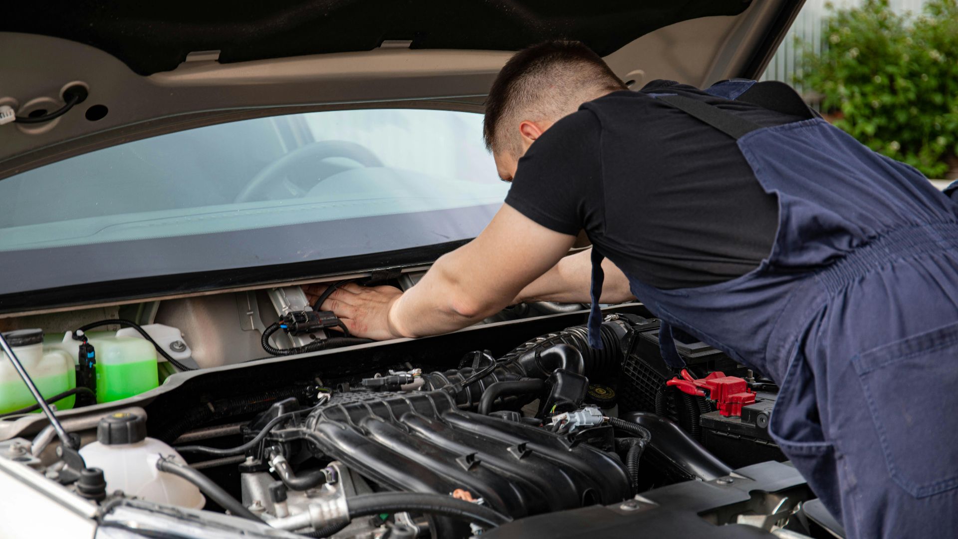 Auto mechanic performs engine maintenance on a car. Focus on hands and engine components.