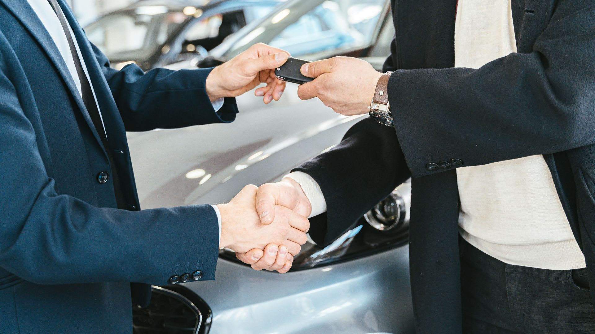 Two businessmen shaking hands and exchanging car keys in a dealership. Symbolizes a successful deal.