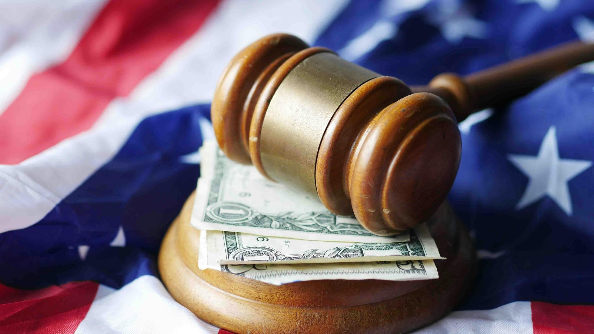A gavel resting on dollar bills atop the American flag, symbolizing justice and finance.