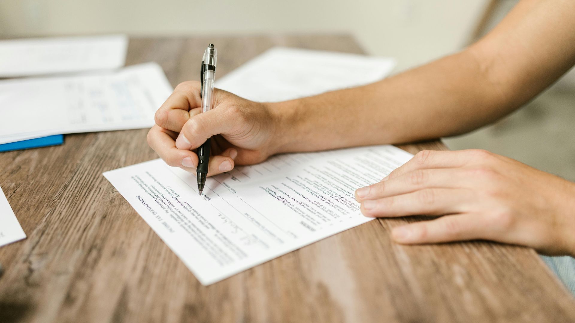 Hand filling out paperwork with a pen, showcasing focus on document completion.