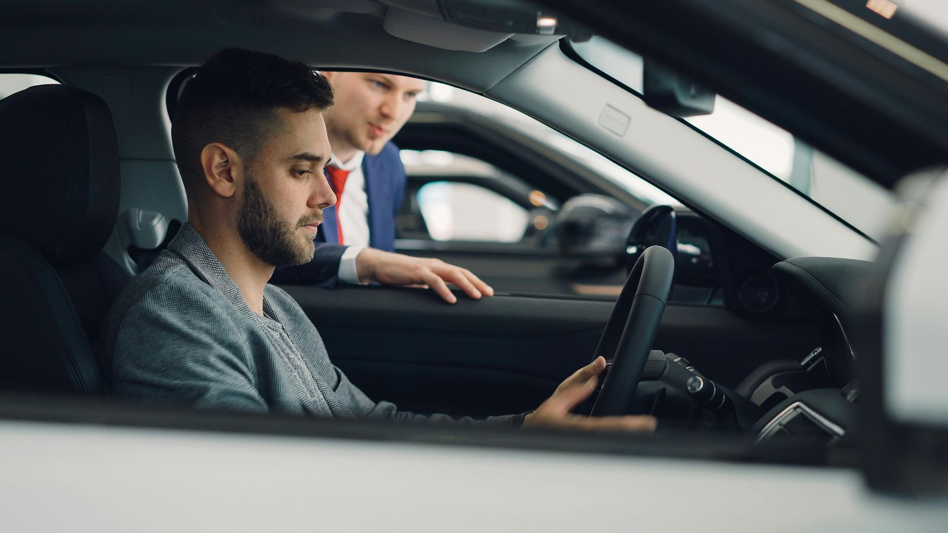 Man examining car interior with salesman at a dealership, highlighting car features.