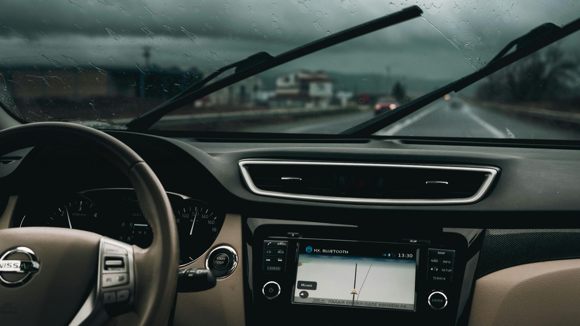 Interior view of a car on a rainy road, capturing steering wheel and dashboard.