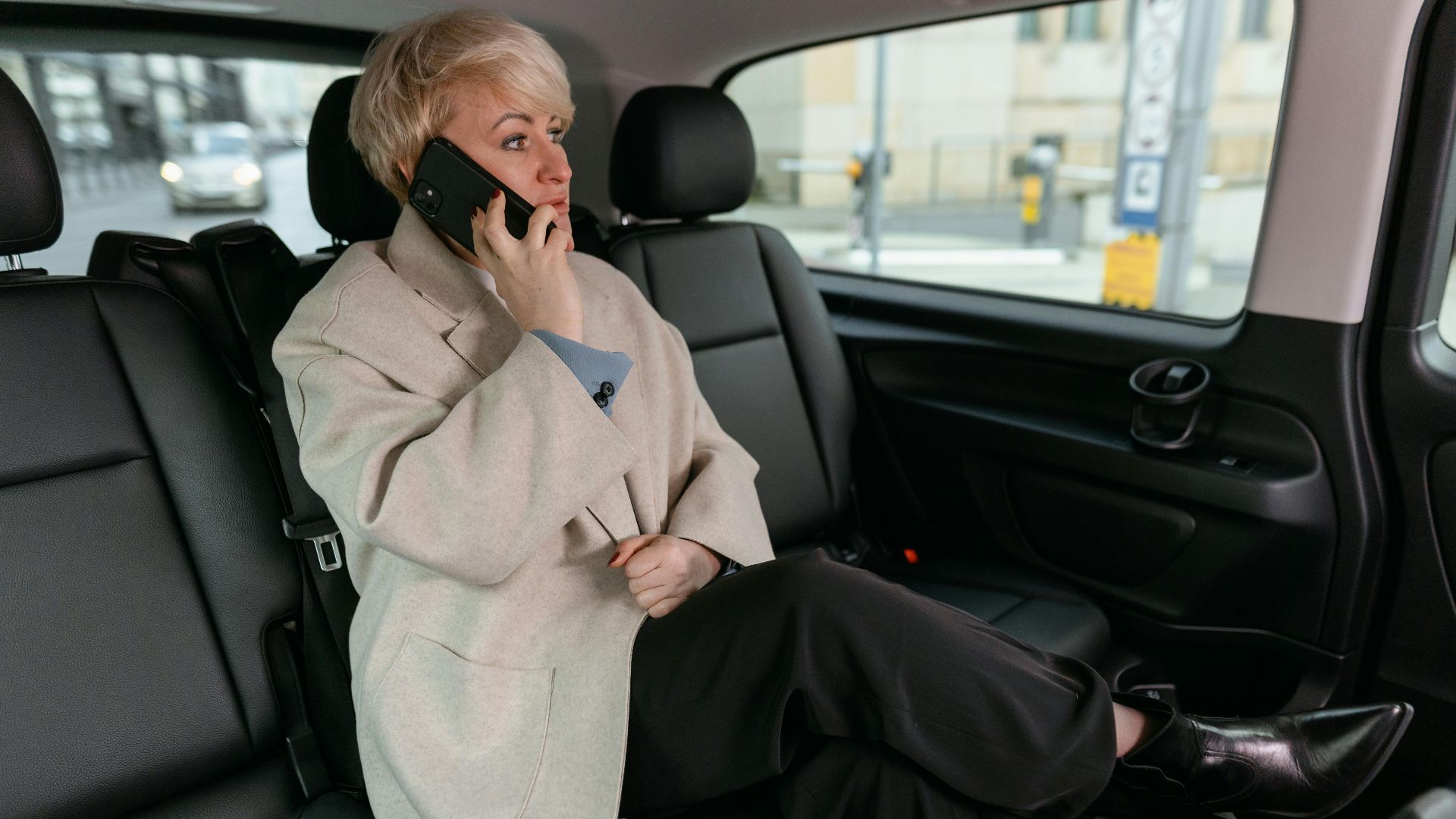 Woman in a car making a phone call, wearing a coat and resting comfortably.