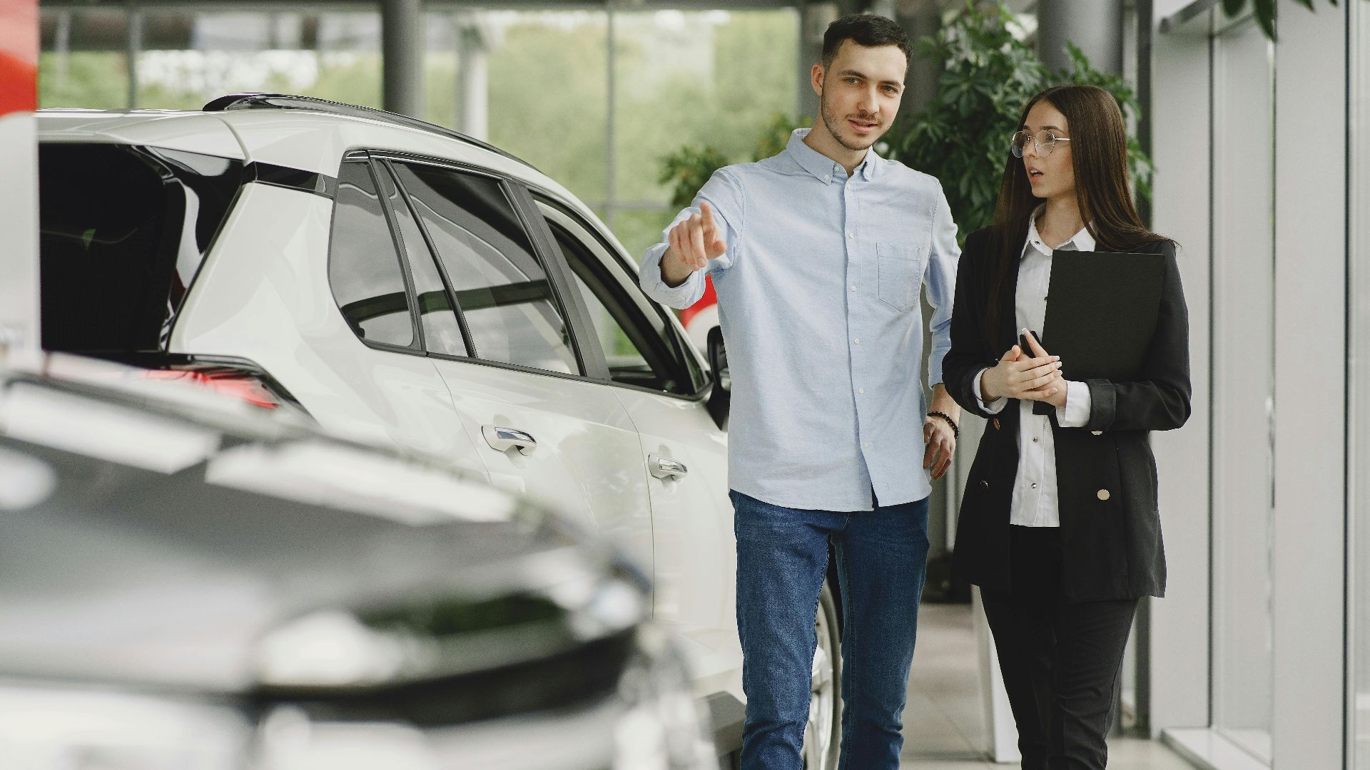 Customer and salesperson discussing a vehicle inside a modern car dealership showroom.
